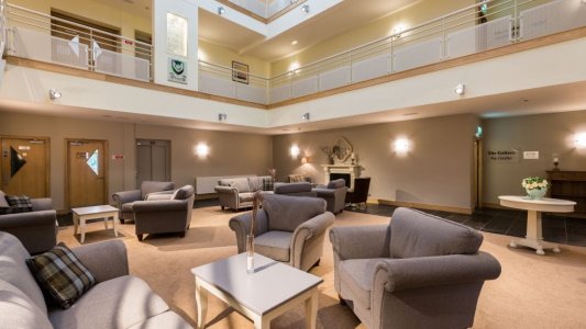 A spacious, well-lit lounge area with multiple sofas and chairs, a fireplace, and a high ceiling with a mezzanine level.