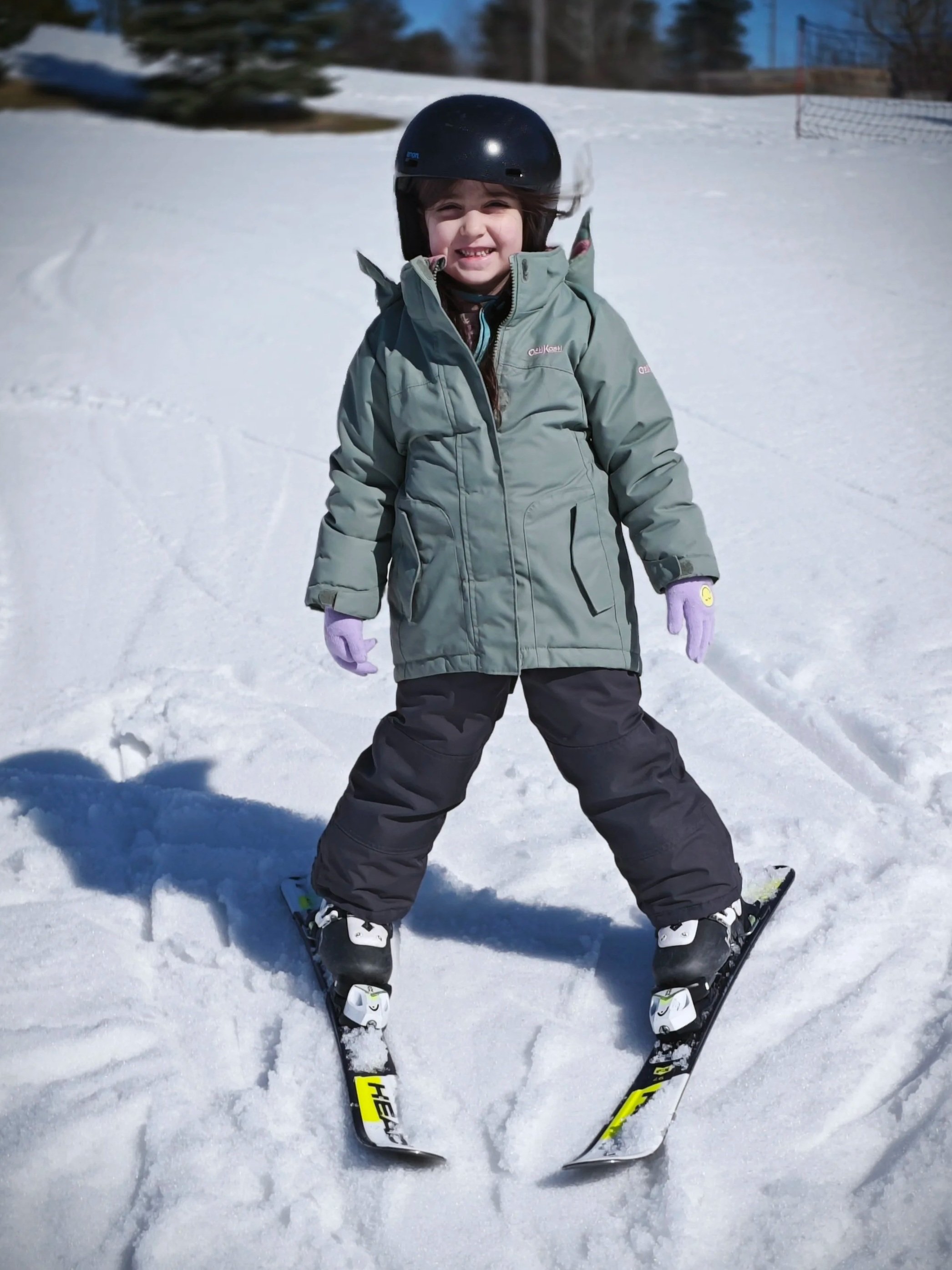 A young girl wearing a helmet and winter clothing on skis in a snowy outdoor setting.