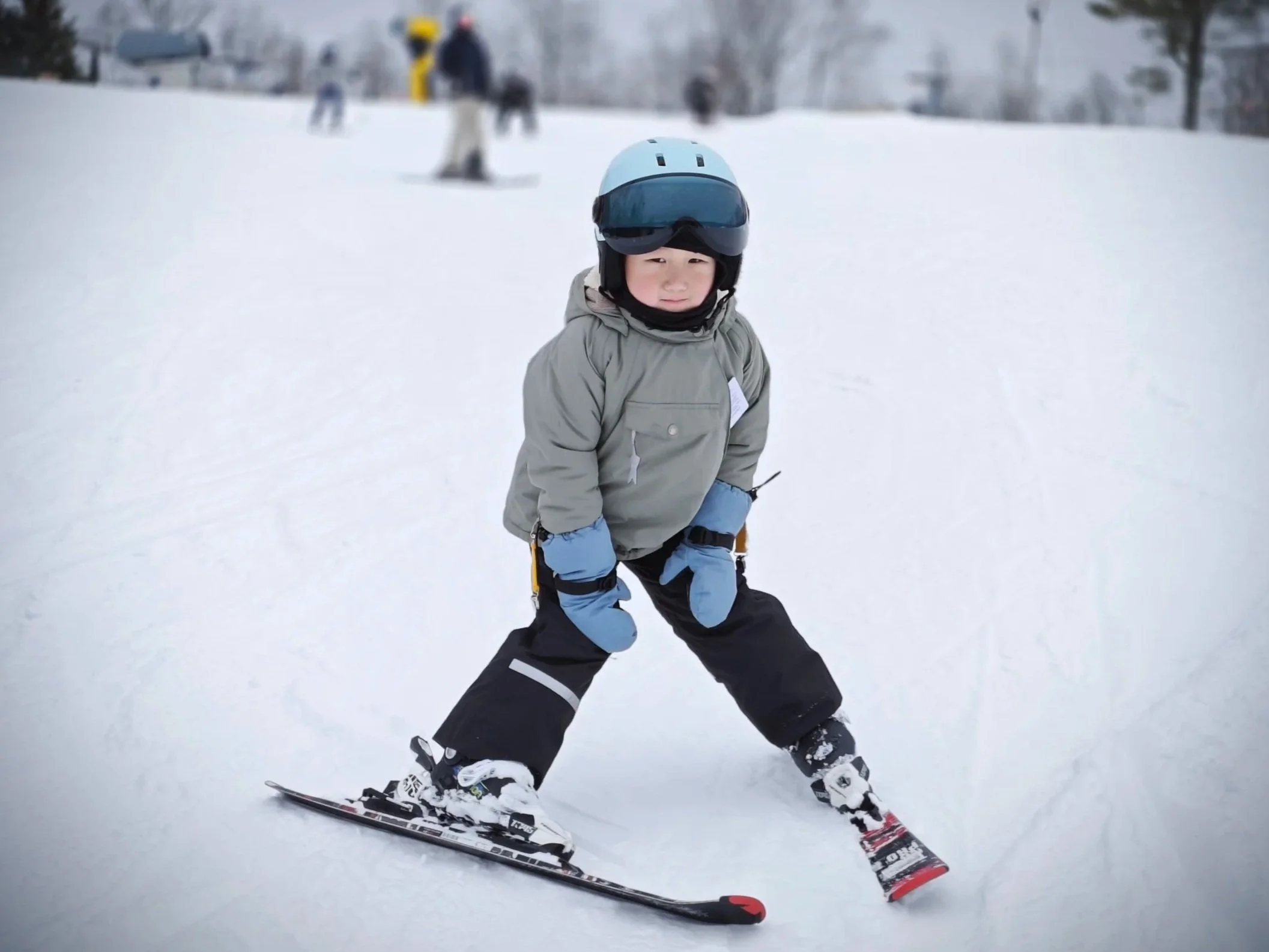 A young child wearing a helmet and winter ski gear skiing on snow with other skiers in the background.