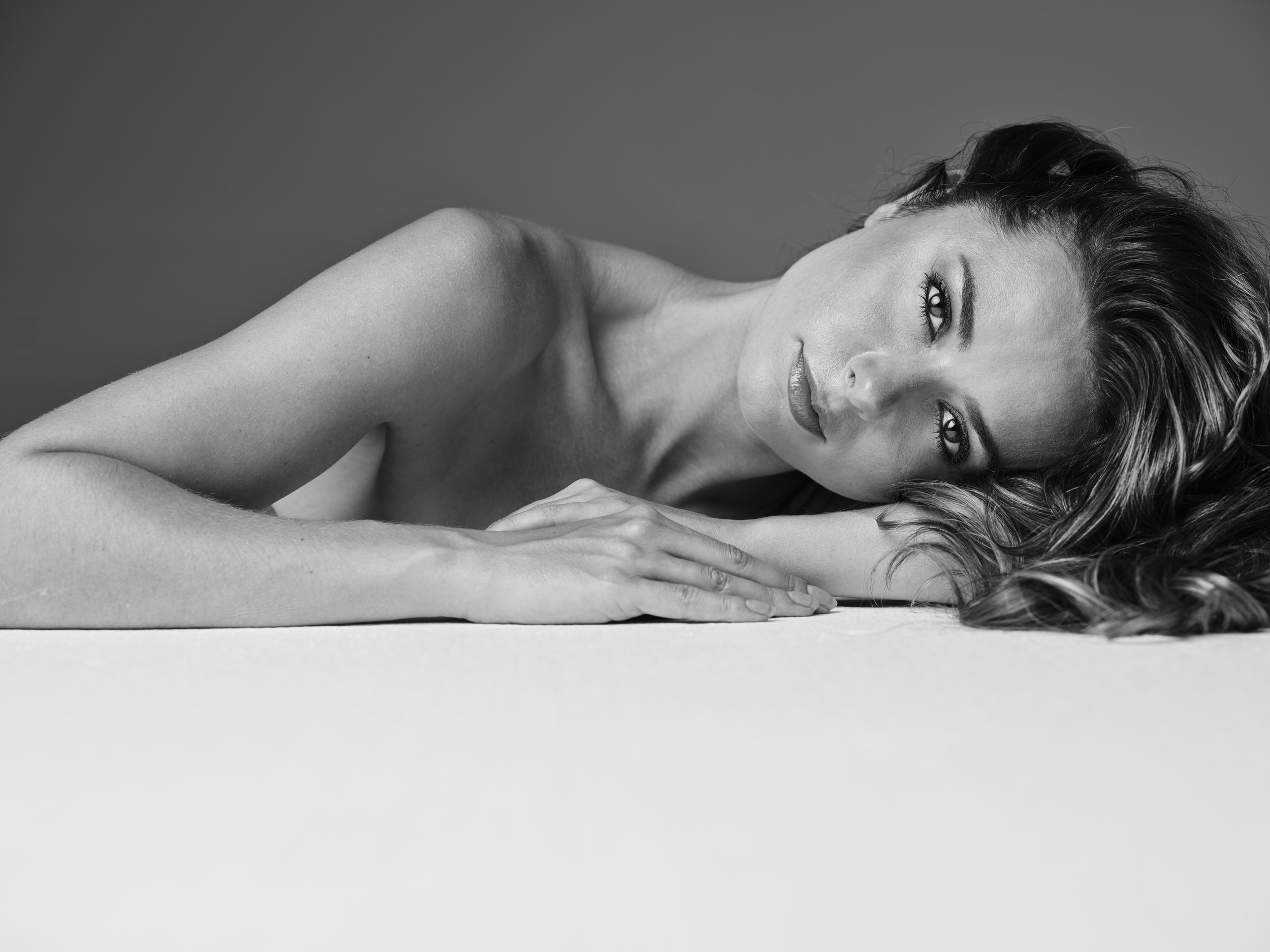 Black and white photo of a woman lying on her side with her head resting on her arm, looking into the camera with a relaxed expression.