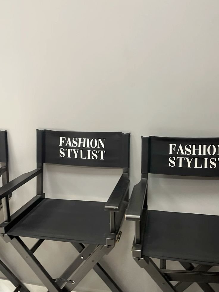 Two black director's chairs with 'Fashion Stylist' written on the backrests, placed against a white wall.