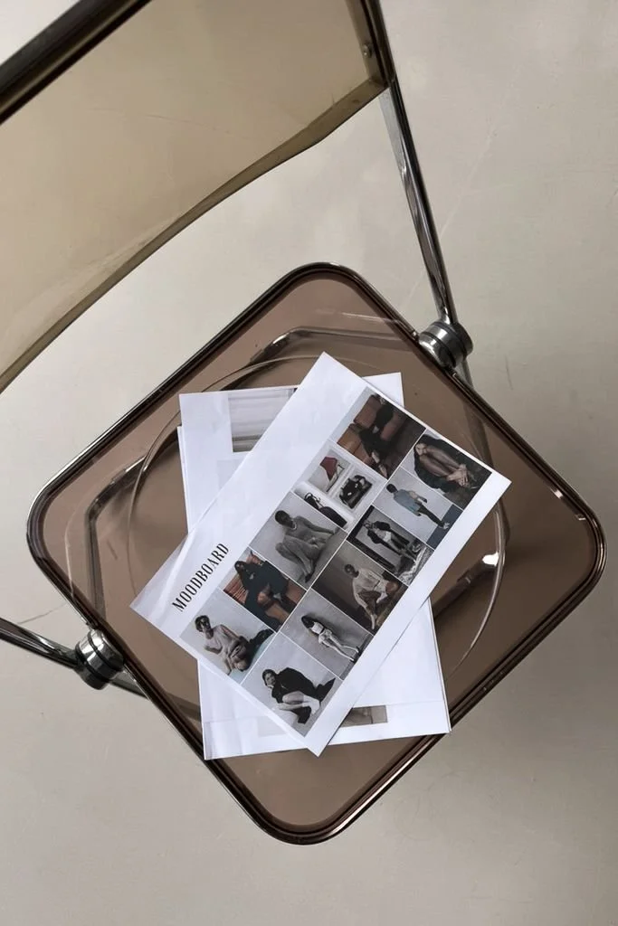 Printed photos of a fashion photoshoot spread out on a glass-top table in a room with white walls.