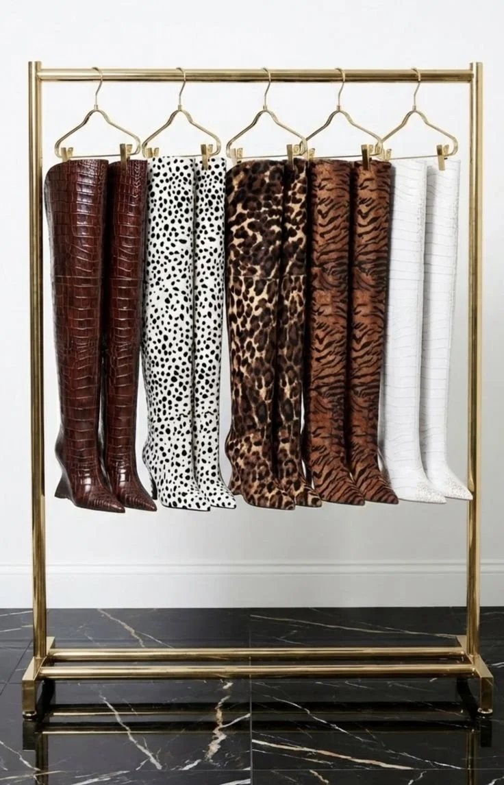 Collection of six pairs of tall boots in various animal print and solid colors hanging on a gold clothing rack.
