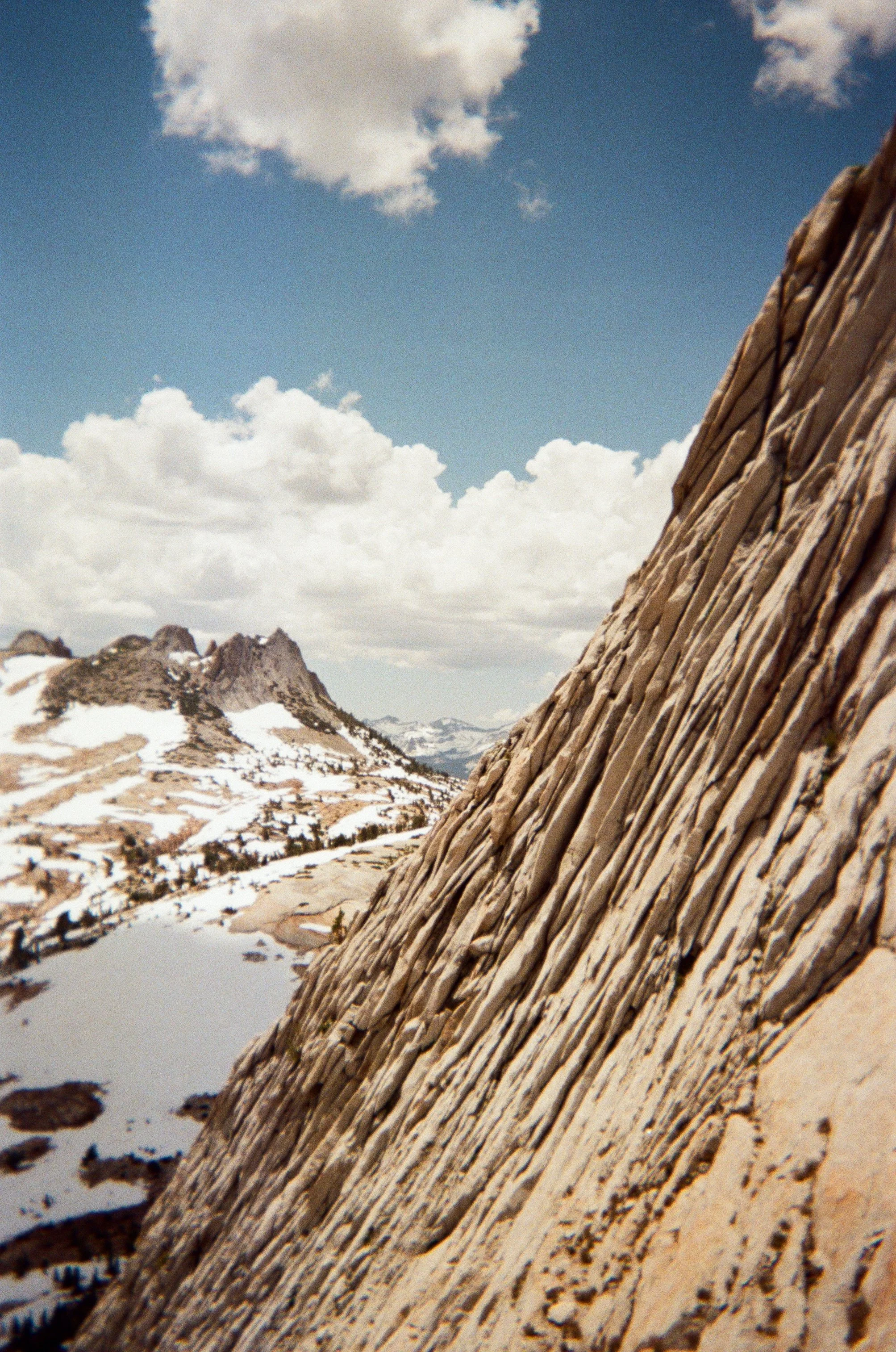Descending back down the hiking trail after rock climbing Cathedral Peak in Yosemite in the summer. Snow covered mountains in the background and rocks in the foreground.  