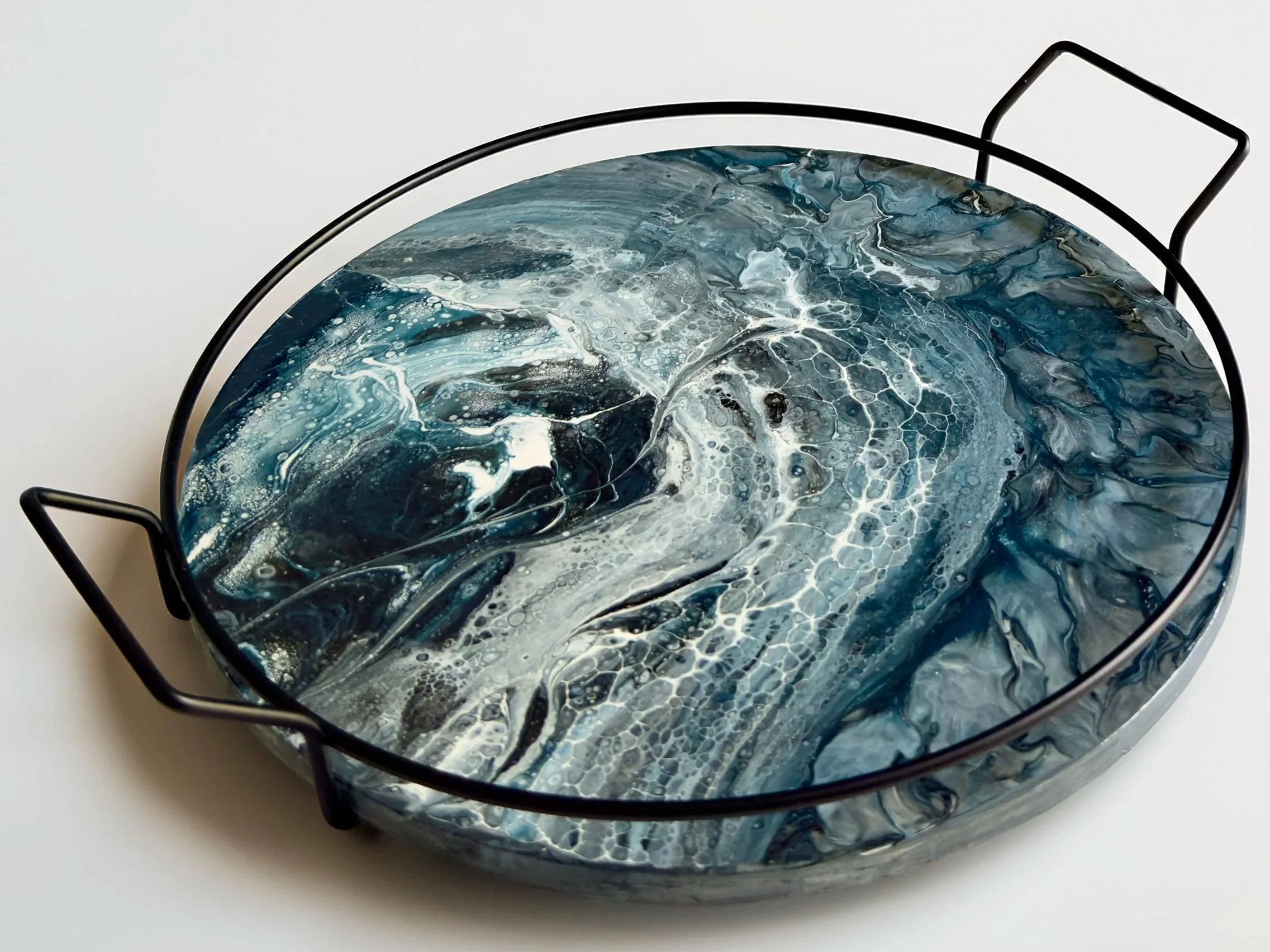 Abstract fluid artwork on a lazy susan featuring layered slate-blue and gray currents flowing through intricate white cellular patterns that resemble water, ice, and shifting tides.