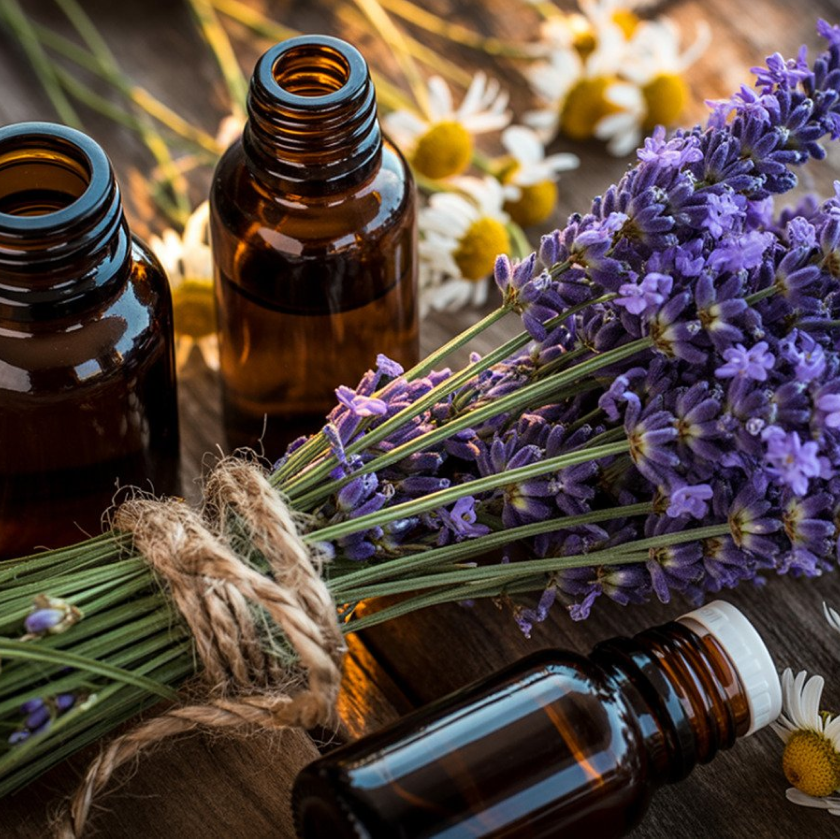 A collection of brown glass essential oil bottles and a bundle of lavender and chamomile flowers on a wooden surface.
