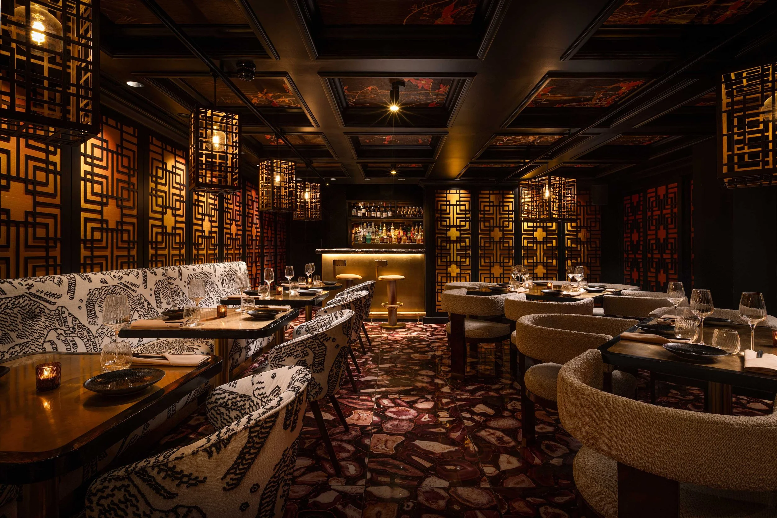 Elegant upscale restaurant interior with patterned walls, plush seating, and a bar with liquor bottles in the background.