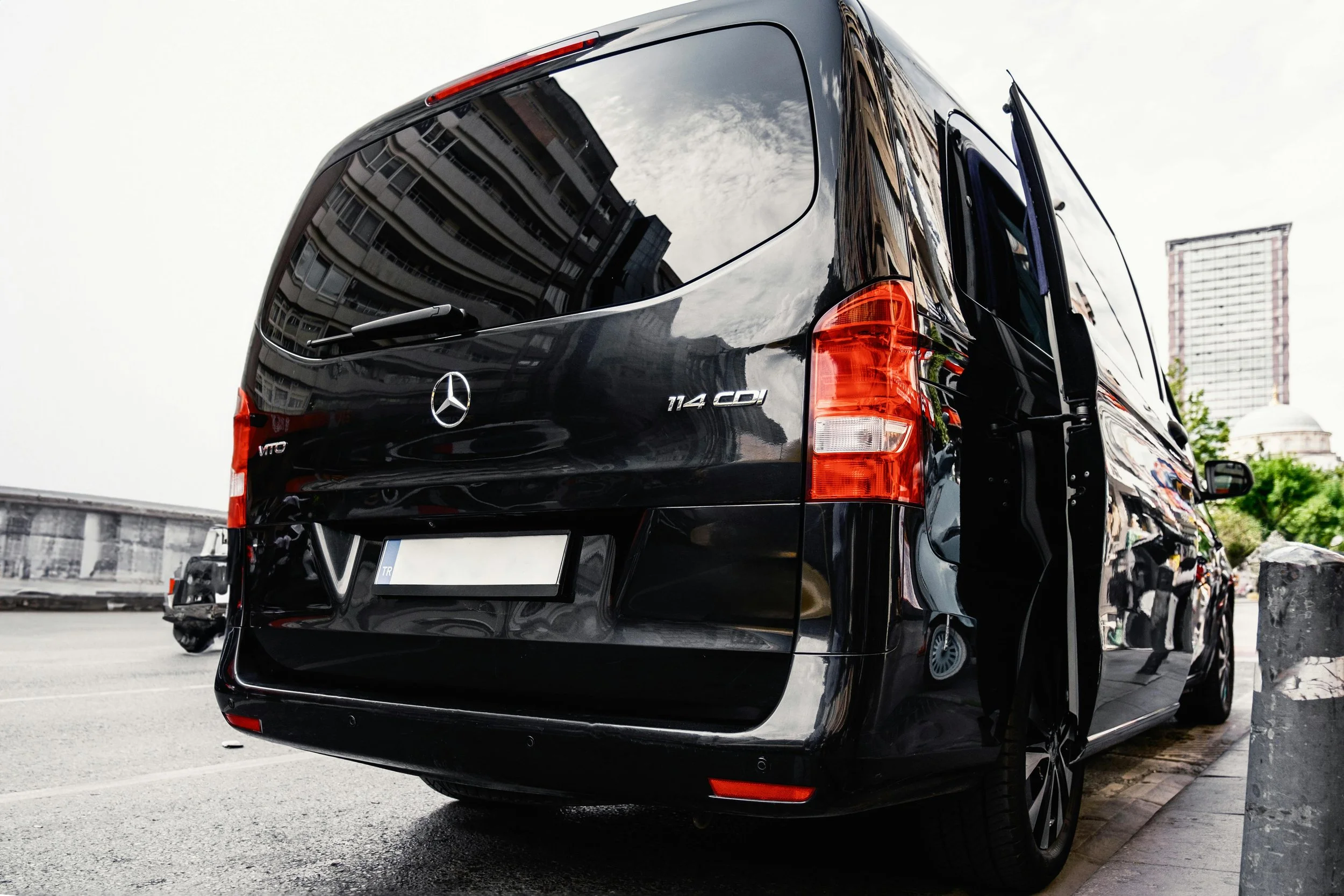 Black Mercedes-Benz Vito van parked on the street, reflecting buildings and cloudy sky on its window.