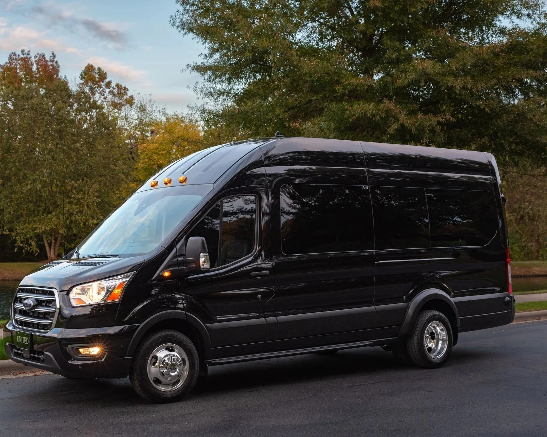 A black cargo van parked on the side of the road with trees and a cloudy sky in the background.