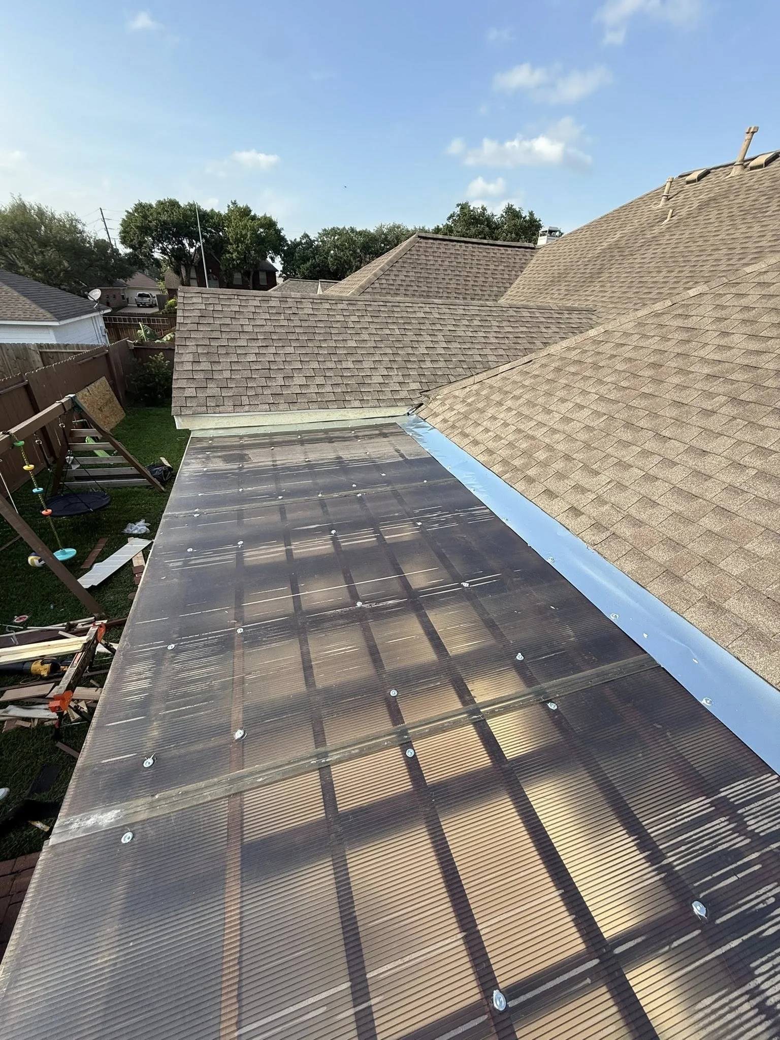 View of rooftops with shingled roofs and a solar panel installation in a neighborhood on a clear, sunny day.