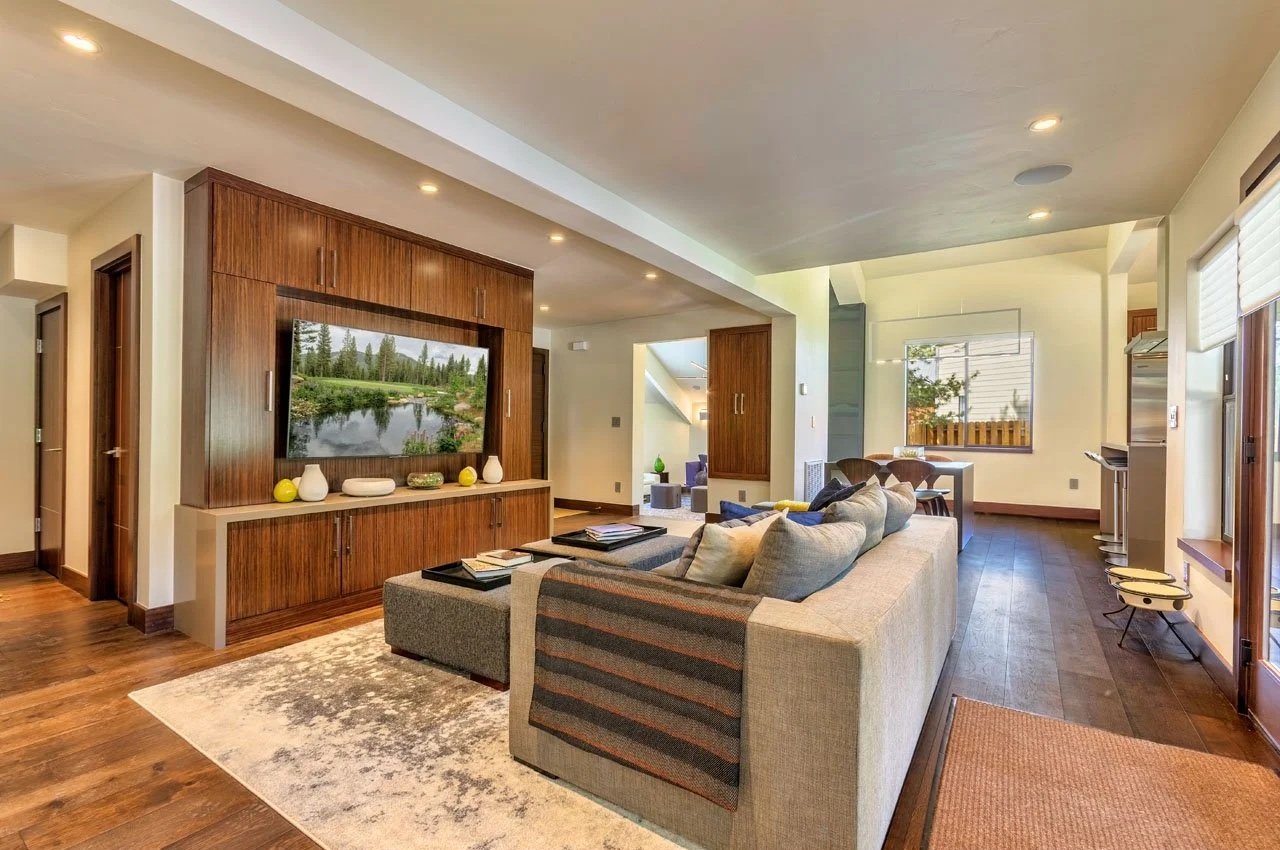 Spacious living room with a large beige couch, wooden built-in entertainment center with a TV, a rug, and several windows letting in natural light.