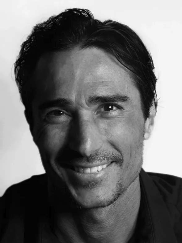 Black and white portrait of a man smiling with short, wavy hair, wearing a dark shirt.
