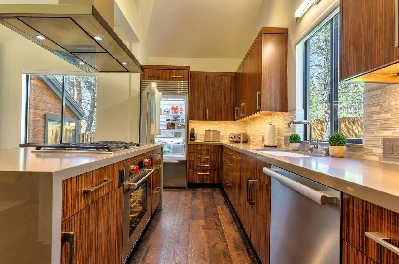 Modern kitchen with wooden cabinets, white countertops, a window with a view of trees, a refrigerator, and various appliances.