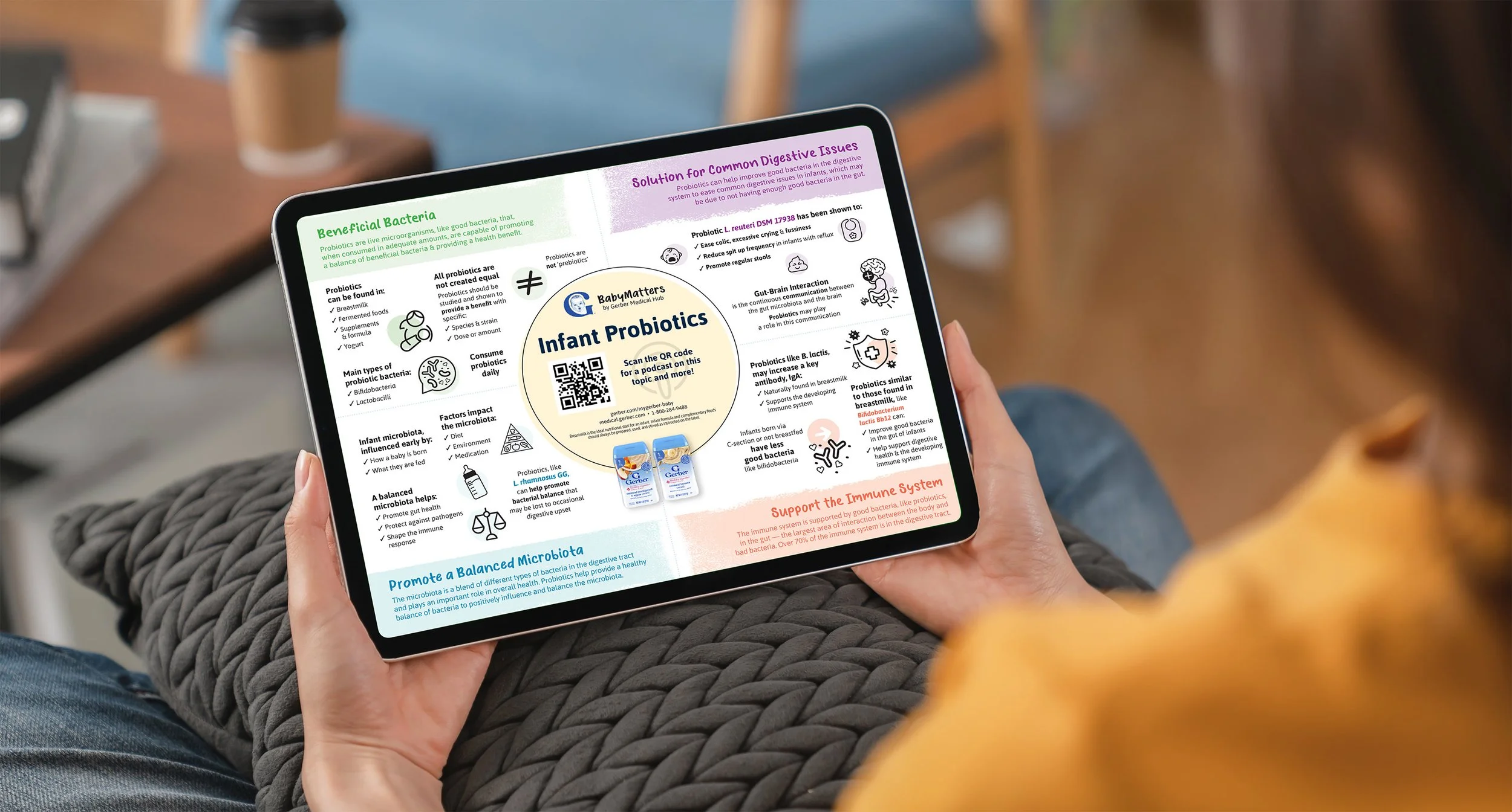 A person holding a tablet displaying an infographic about infant probiotics, including information on beneficial bacteria, probiotic types, factors impacting microbiota, and supporting the immune system, with a QR code for more details.