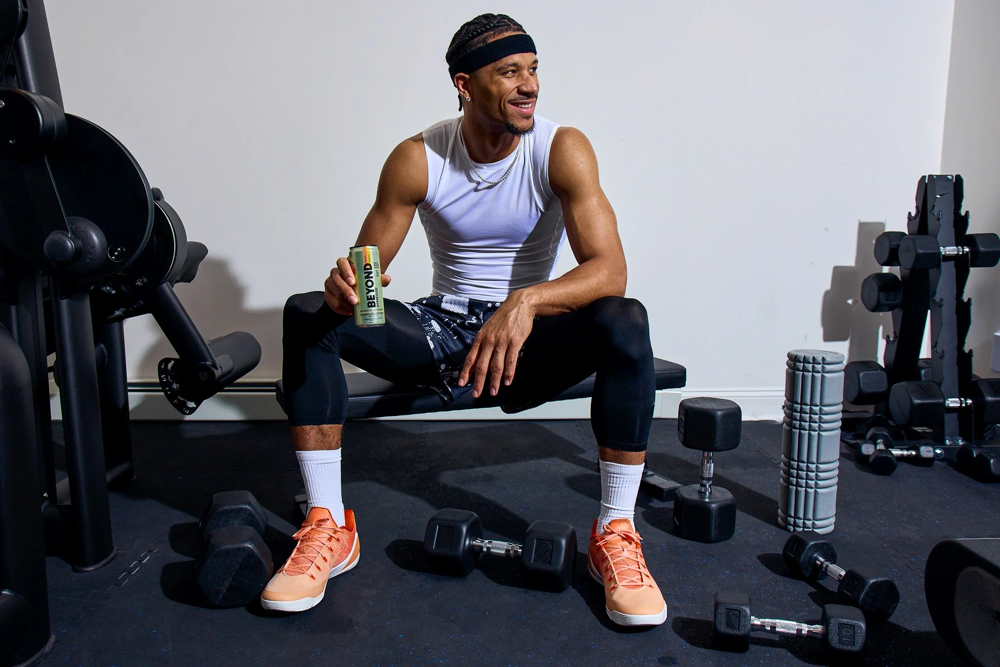 A man sitting in a home gym, holding a can of Beyond energy drink, surrounded by workout equipment including dumbbells and foam rollers.