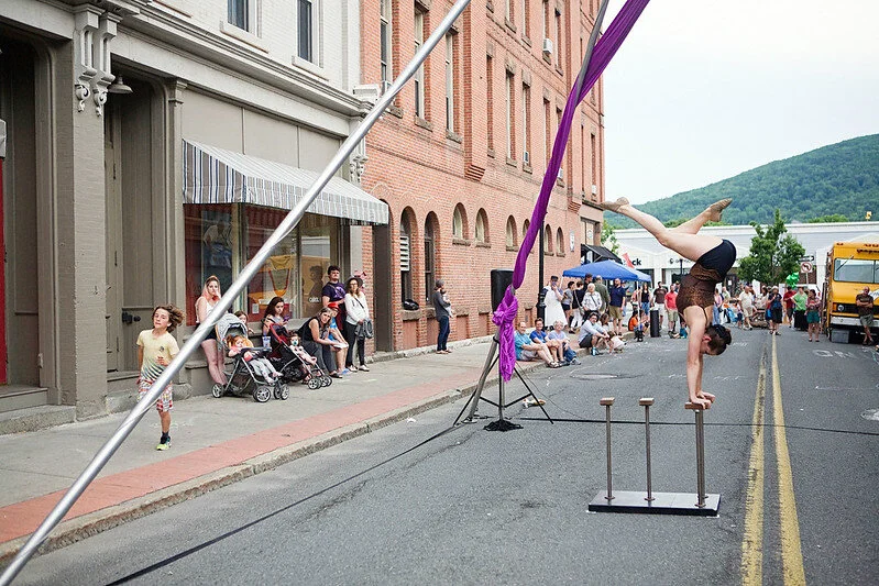 a woman is balancing on her hands as part of a circus performance on a small-town street.