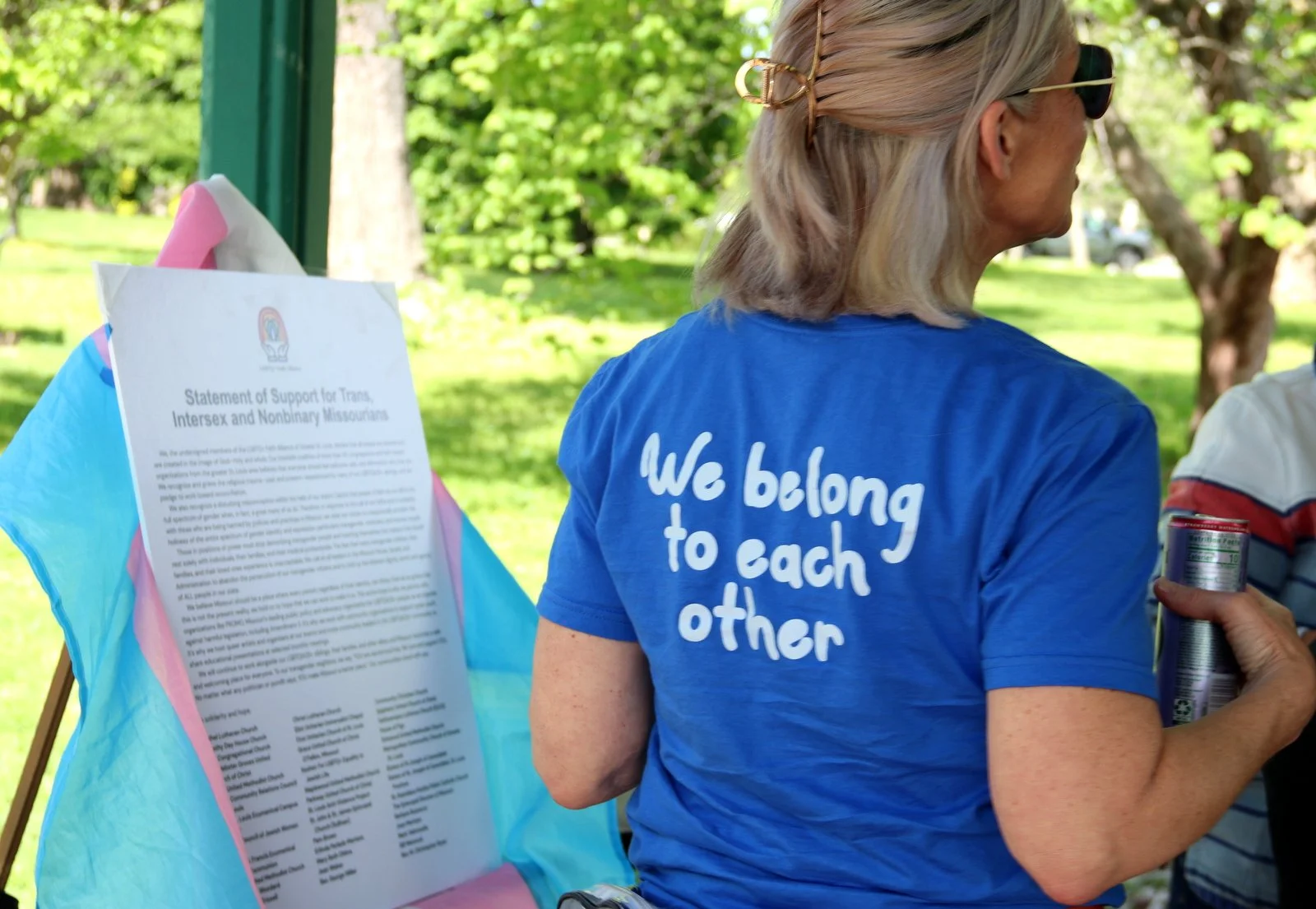 Someone standing, wearing a "We Belong To Each Other" shirt, in front of the Statement of Support.