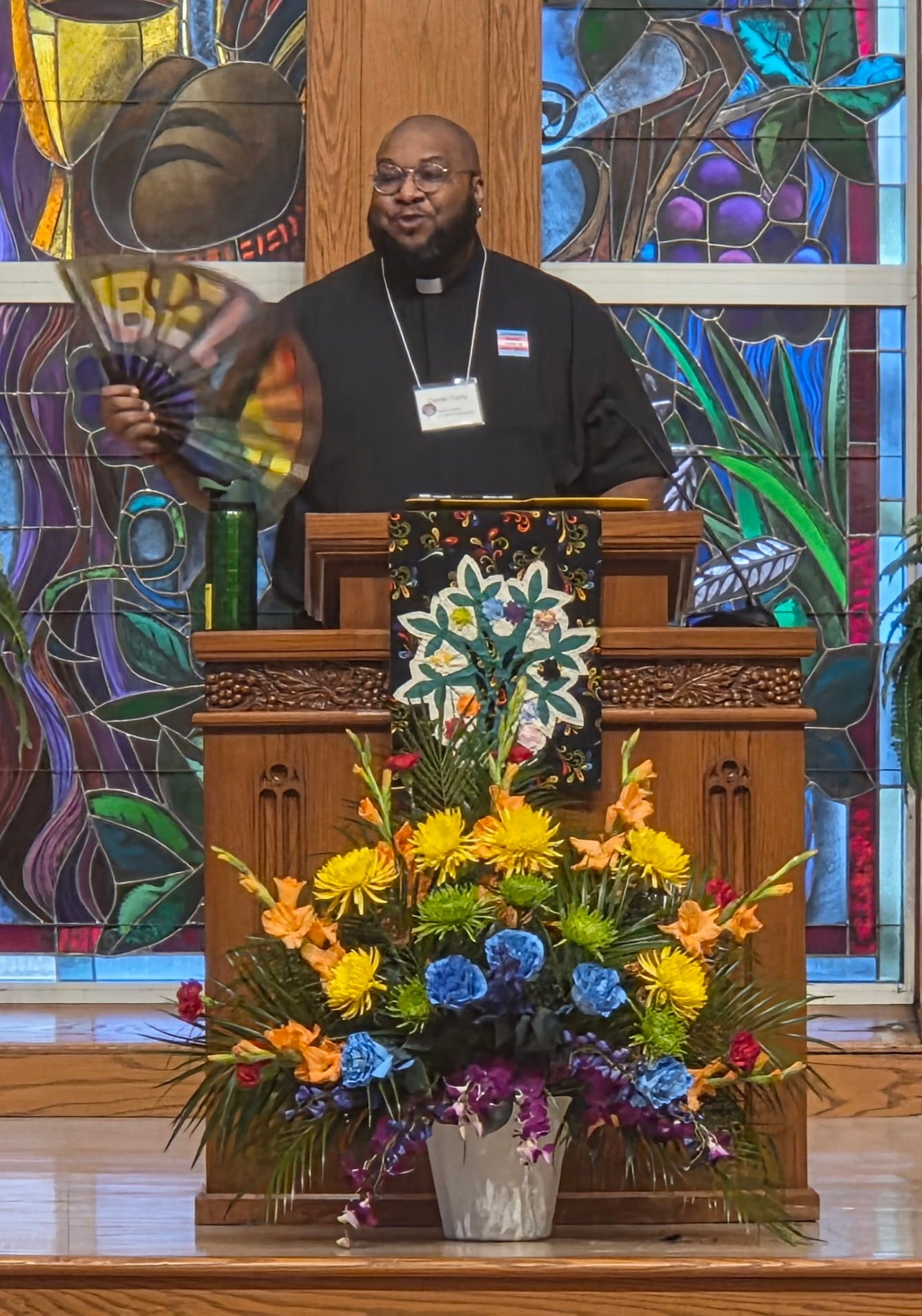 Someone standing at a pulpit, preaching, holding a rainbow fan.