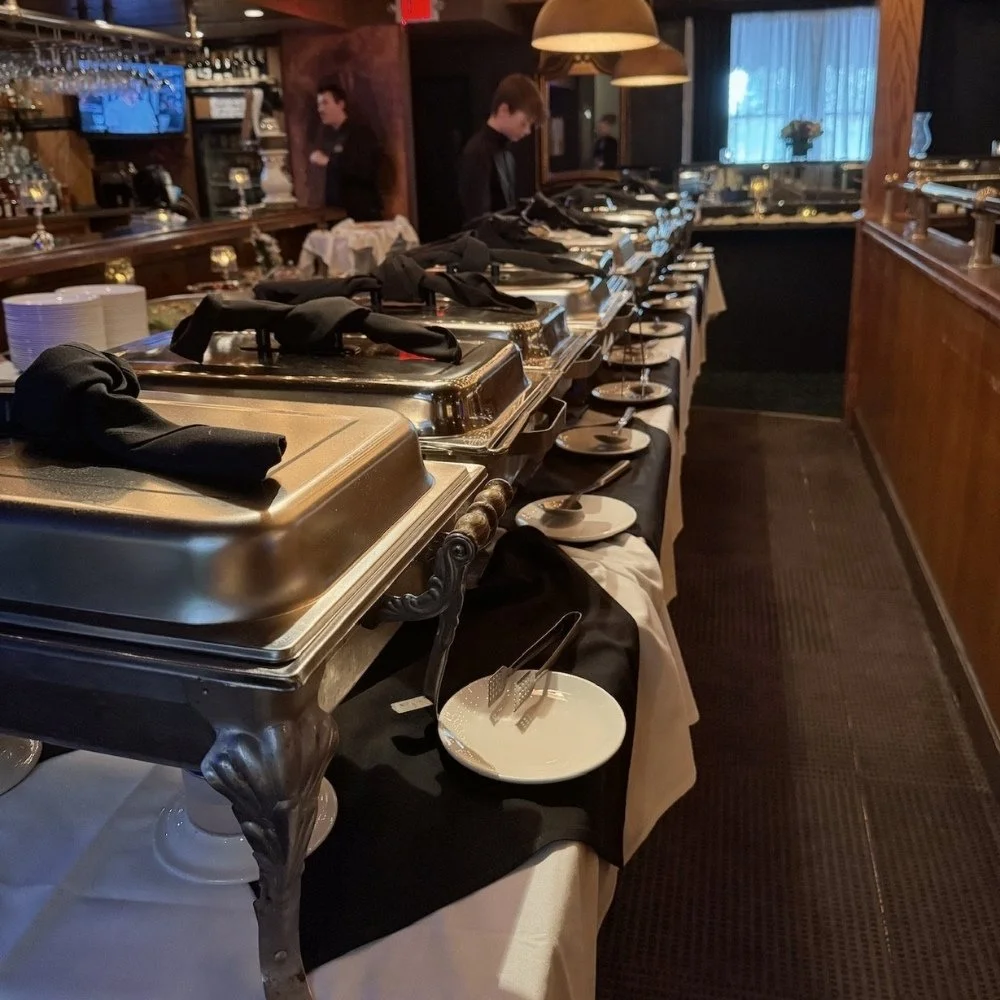 Sam's buffet table with domed food covers, white plates, and black napkins.