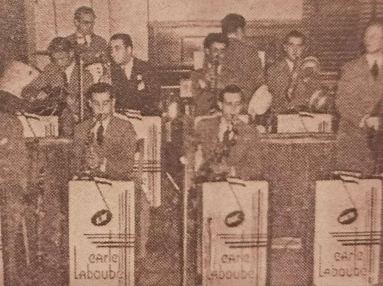 A group of men in suits playing in a bandstand in the banquet room.