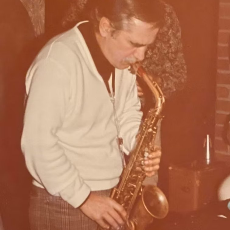A man who is playing saxophone for Sam Andria in a dimly lit room.