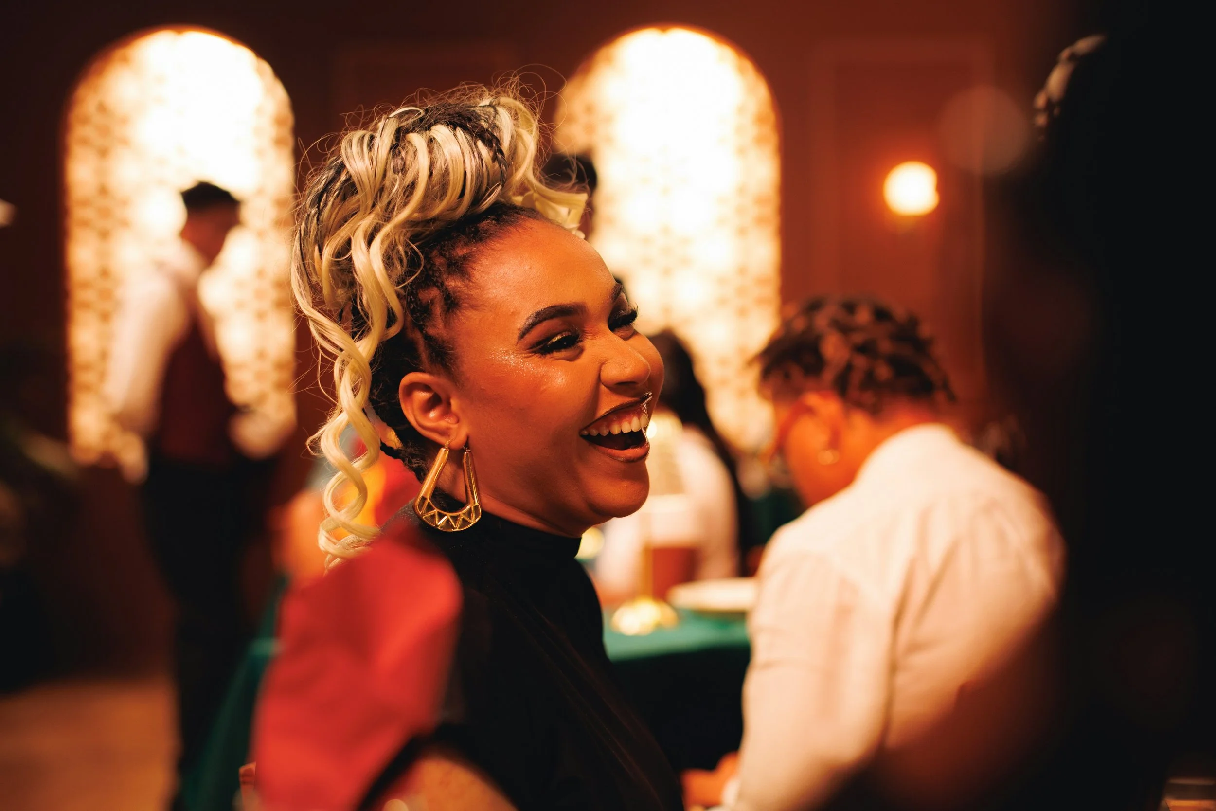 Women with styled hair and earrings smiling at an indoor gathering or party.