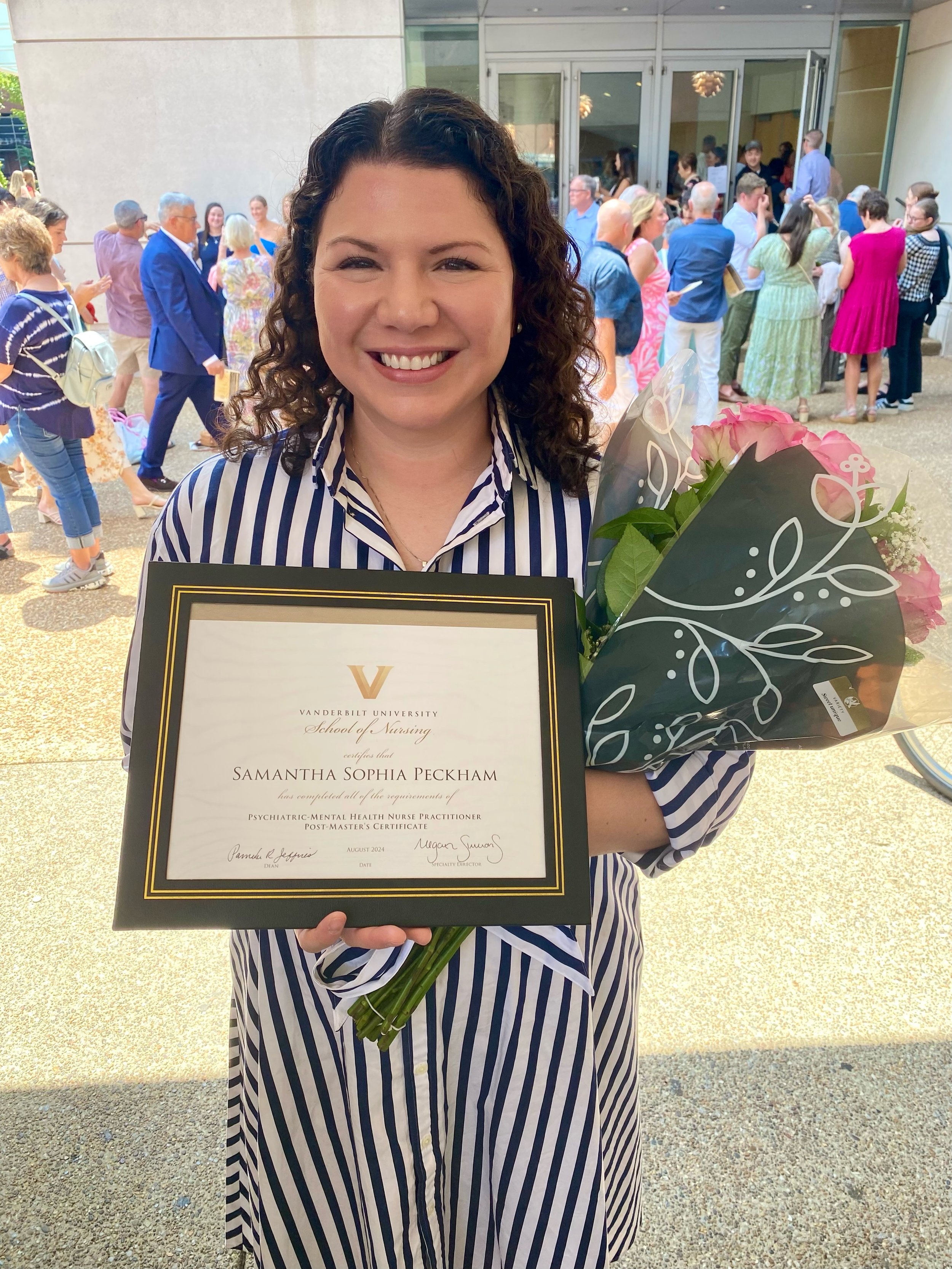 Woman smiling and holding a diploma and bouquet of pink roses outside a building, celebrating her graduation at Vanderbilt University School of Nursing.