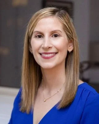 A woman with straight, blonde hair wearing a blue top and smiling at the camera.