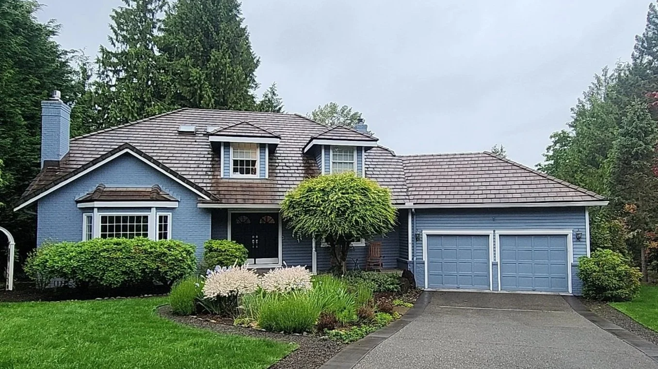 Blue house with brown roof, surrounded by green trees and landscaped garden.