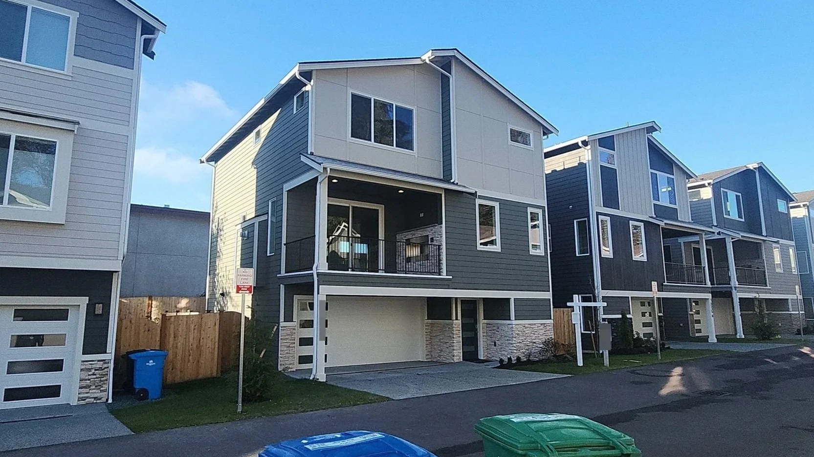 A row of modern multi-story houses with large windows, balconies, and garages, situated on a residential street in clear weather.