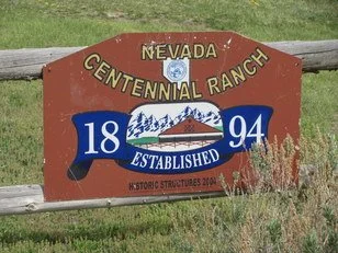 Sign for Nevada Centennial Ranch, established in 1894, featuring mountains and trees, with an American flag emblem.