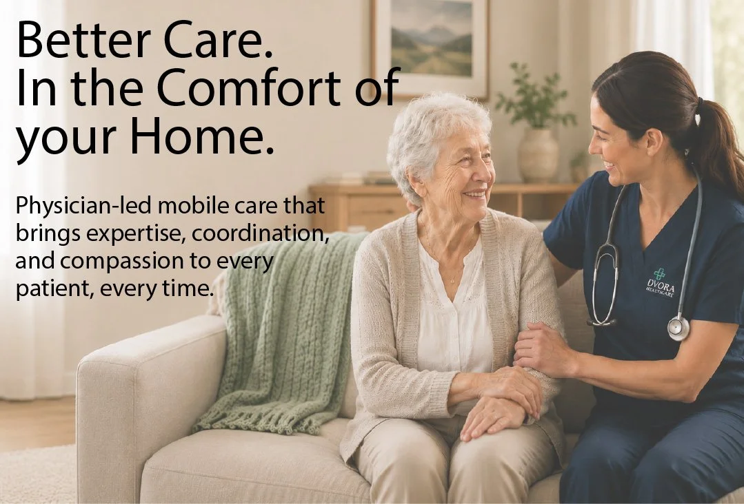 A healthcare professional, wearing a navy uniform with a stethoscope around her neck, smiles and holds hands with an elderly woman sitting on a beige couch. The room has warm lighting, a framed picture, and a green blanket on the couch.