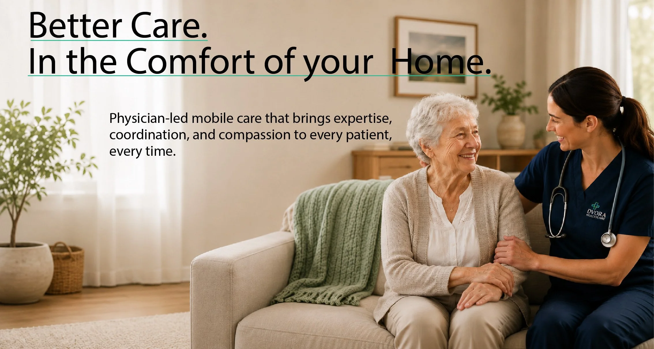 A healthcare professional, wearing navy scrubs and a stethoscope, talking to an elderly woman sitting on a sofa in a well-lit living room. The living room has neutral tones, a large potted plant, and framed artwork on the wall.