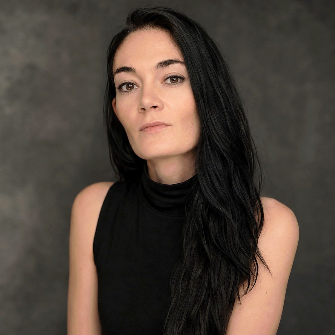 Photo of writer Abigail Moyer with a dark grey studio background. A woman with dark hair and pale skin looking at the camera.