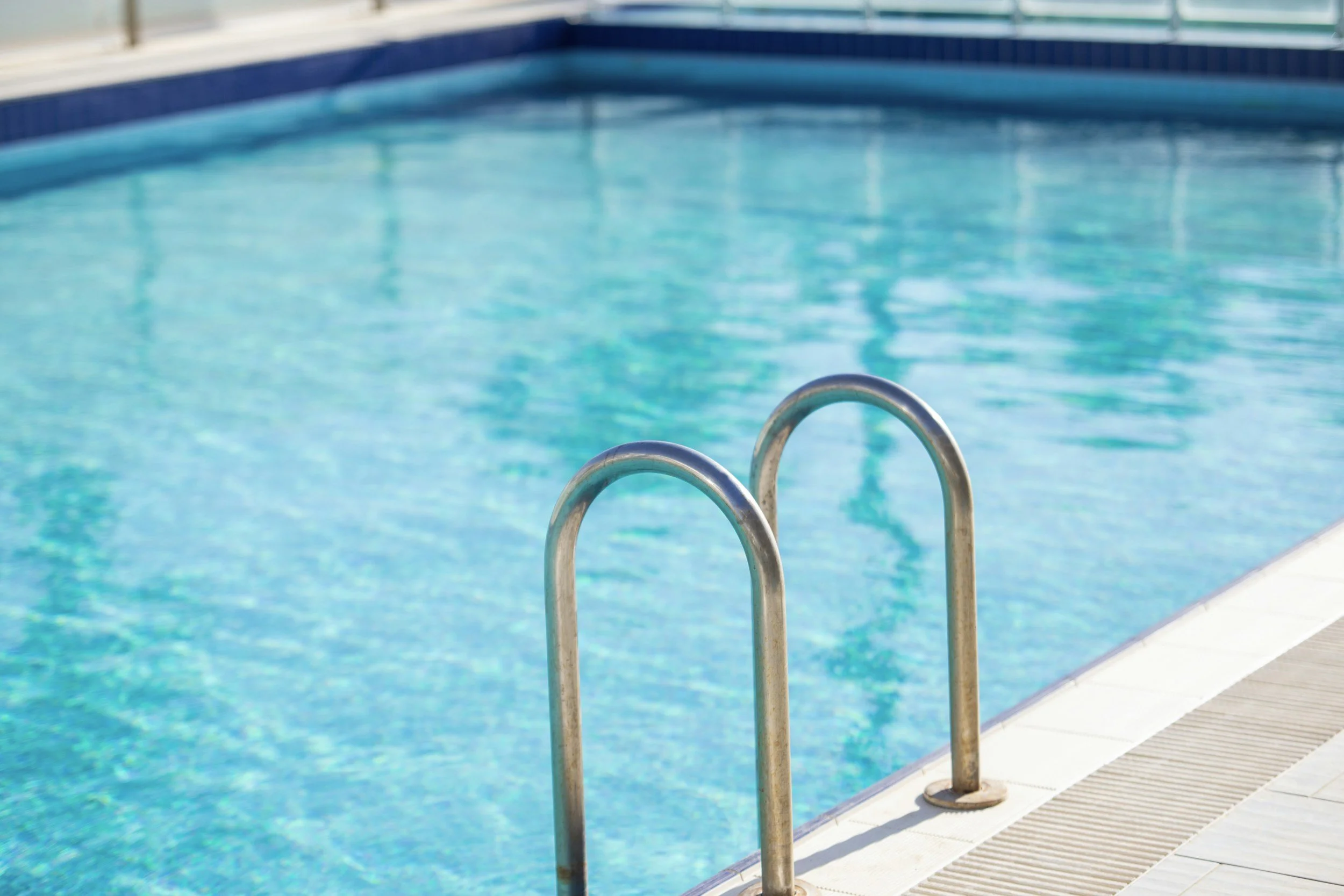 Swimming pool with metal ladder and blue tiles along the edge.