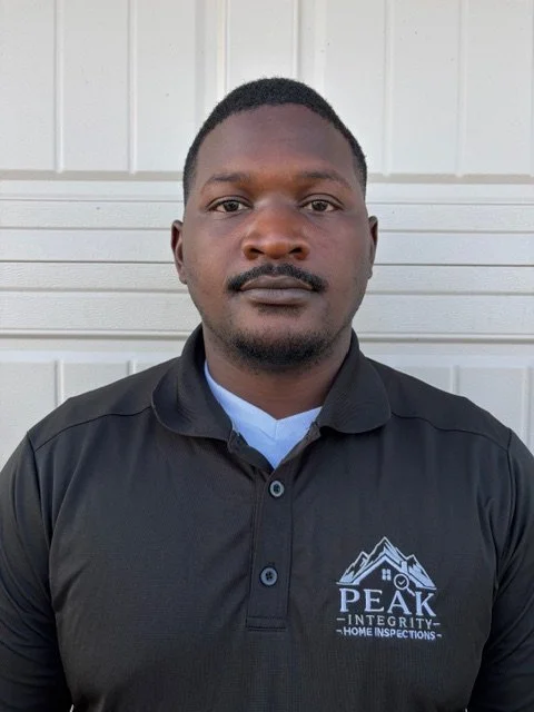 Man wearing a black polo shirt with a logo that reads 'PEAK INTEGRITY HOME INSPECTIONS' in front of a white garage door.