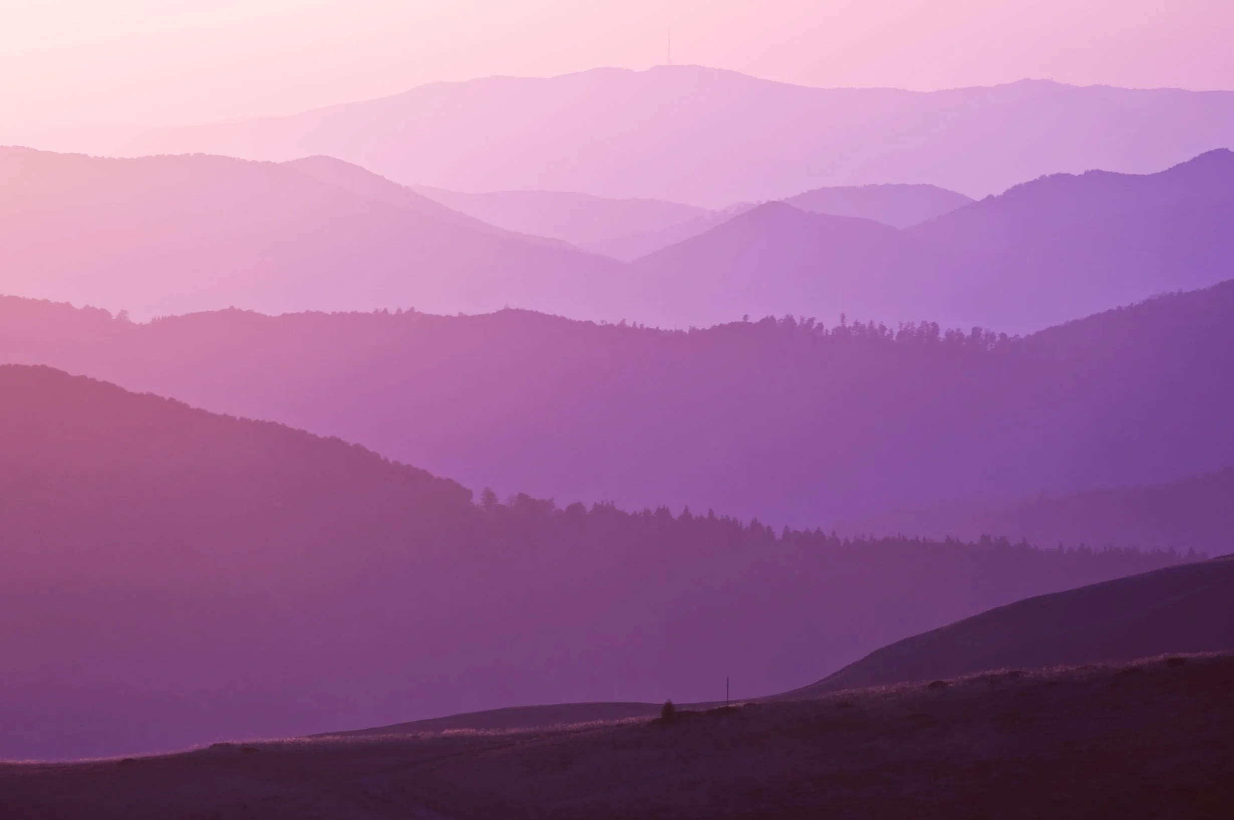 A mountain landscape with multiple mountain ridges in shades of purple and pink, with a gradient sky in the background.