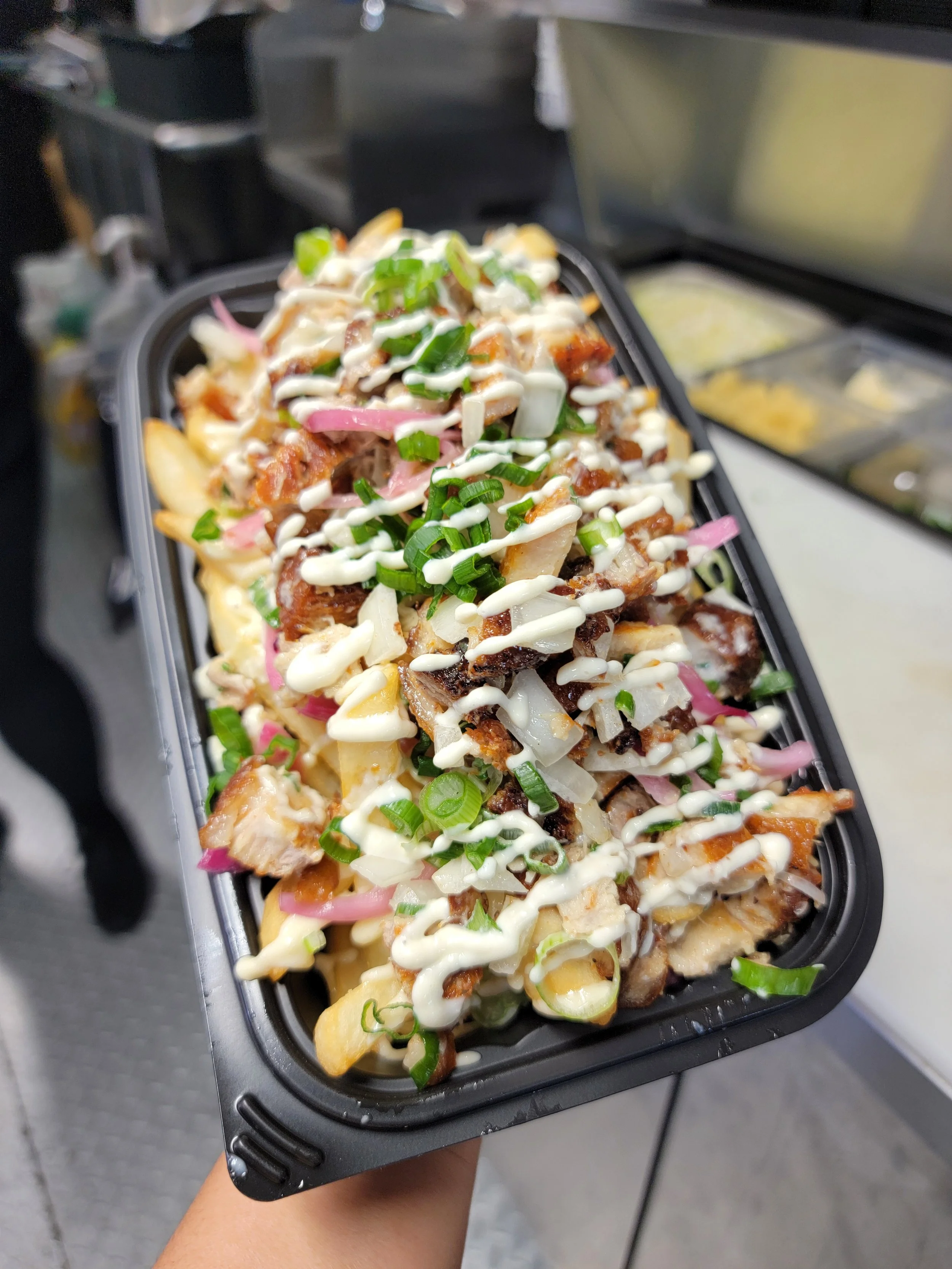 Close-up of a tray of loaded nachos topped with green onions, mayonnaise, and other ingredients.