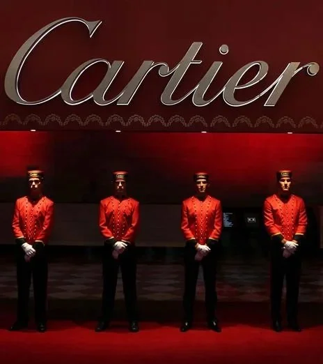 Four uniformed doormen standing in front of a Cartier store with a red background and large Cartier sign.