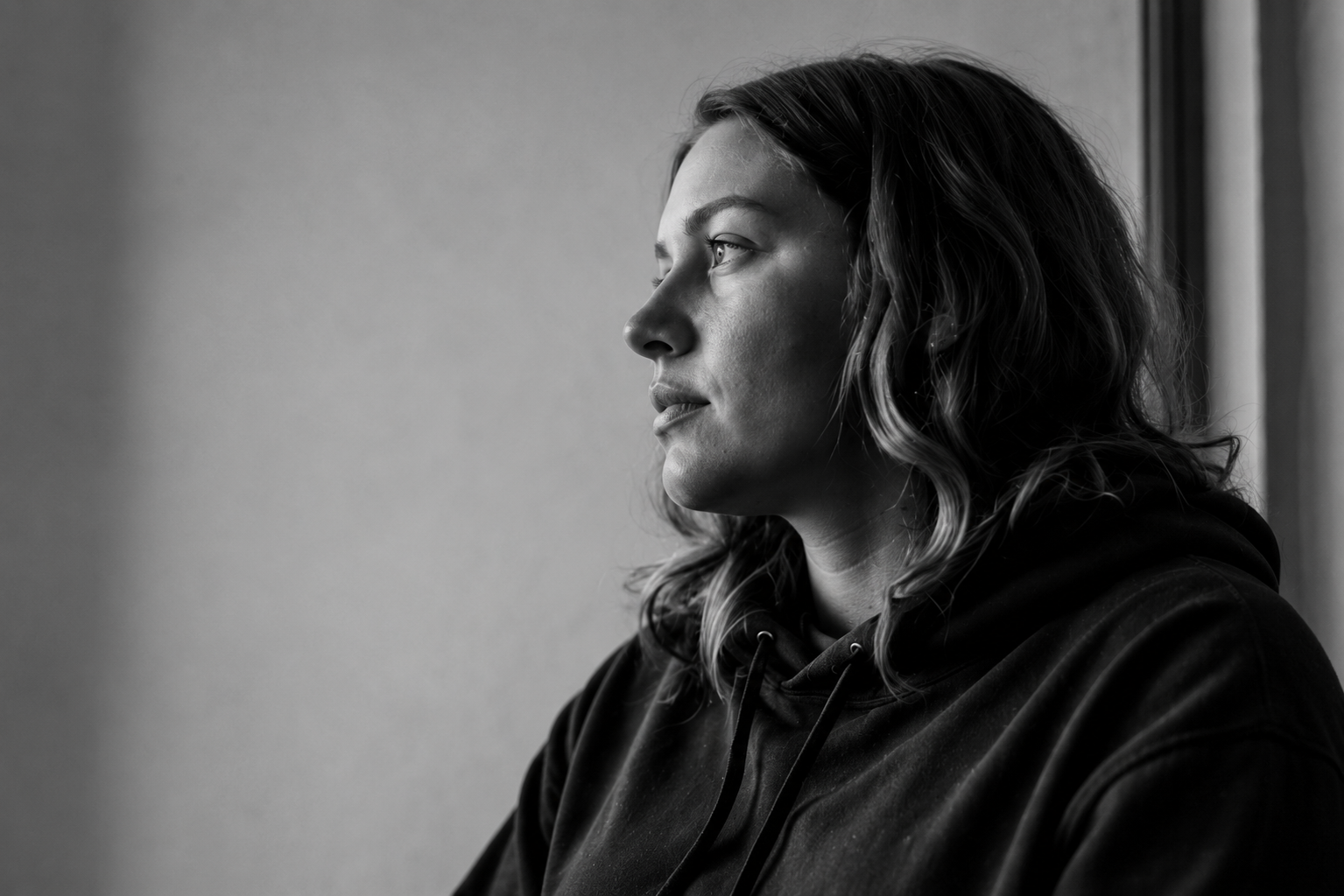 A black and white photo of a woman with wavy hair in profile, looking out a window.