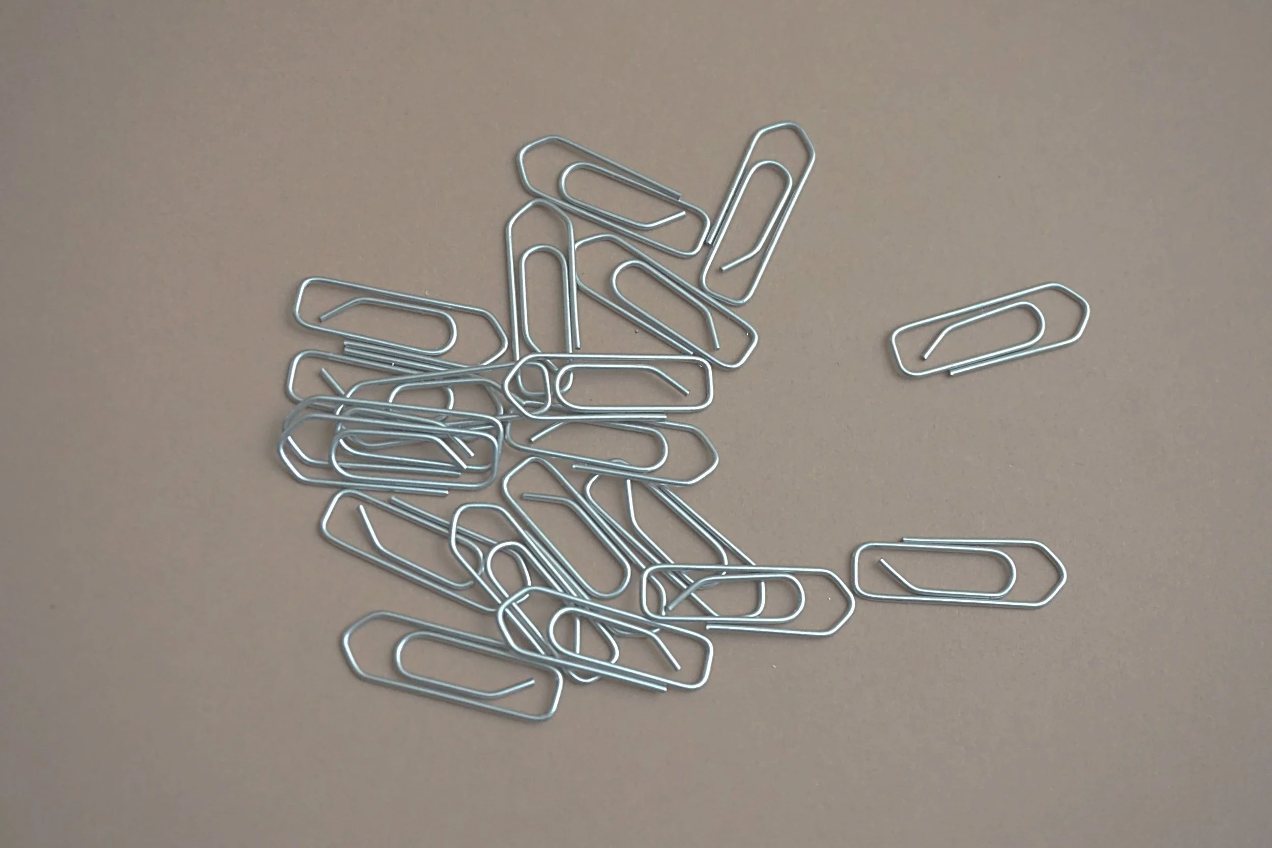 A scattered pile of silver metal paper clips on a beige surface.