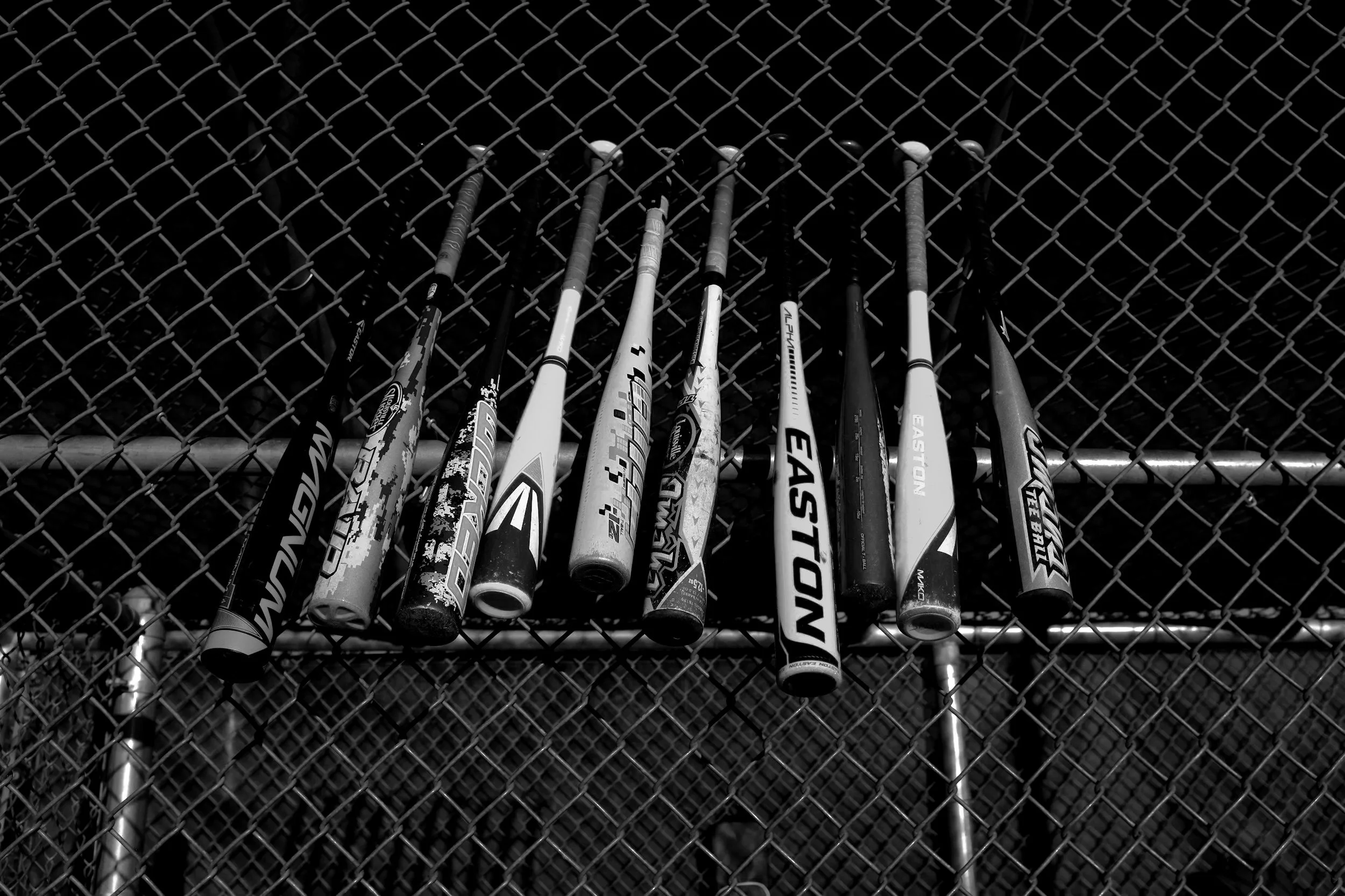 Multiple baseball bats hanging on a chain-link fence.