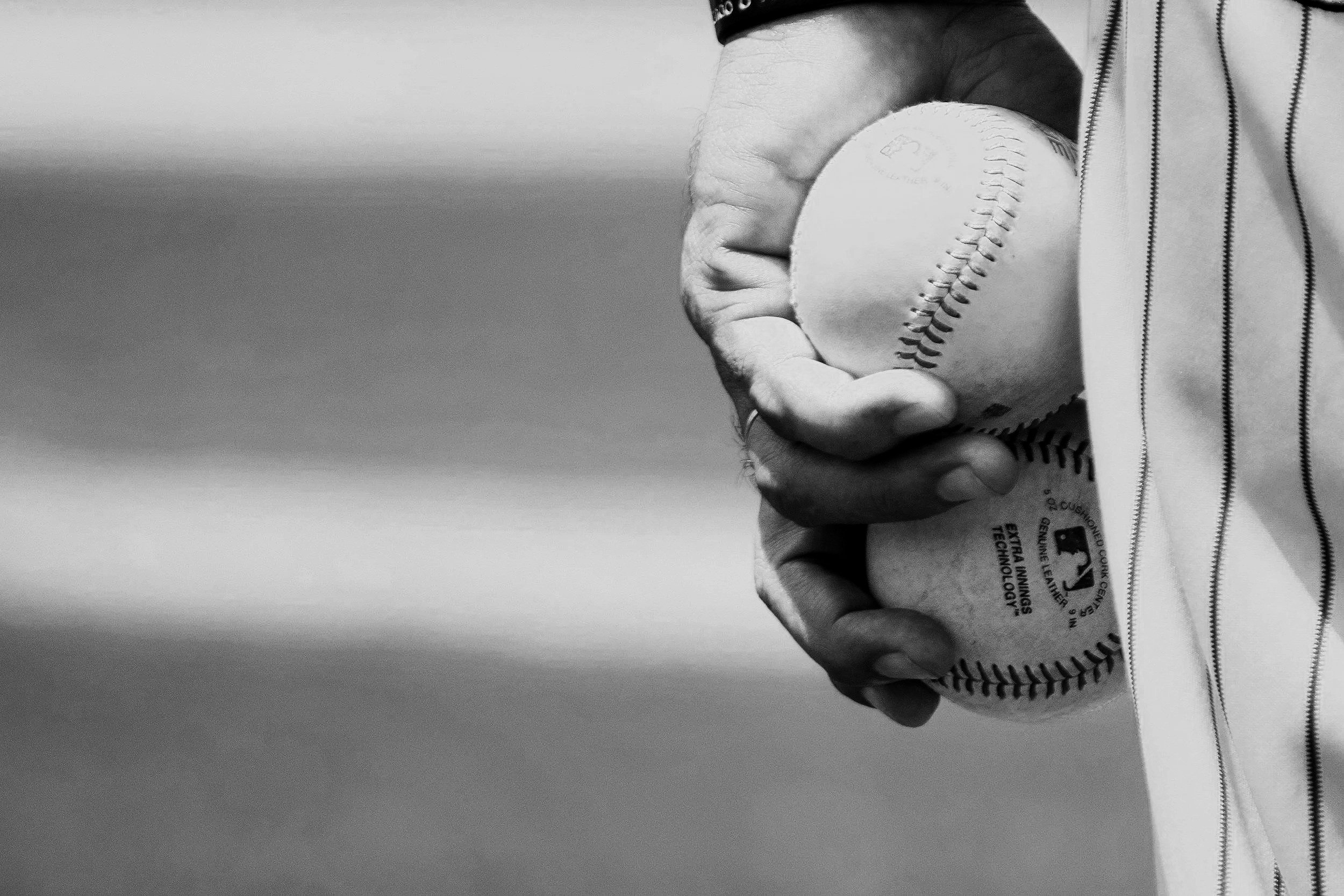 A person holding a baseball with their right hand, wearing a striped pants against a plain background.