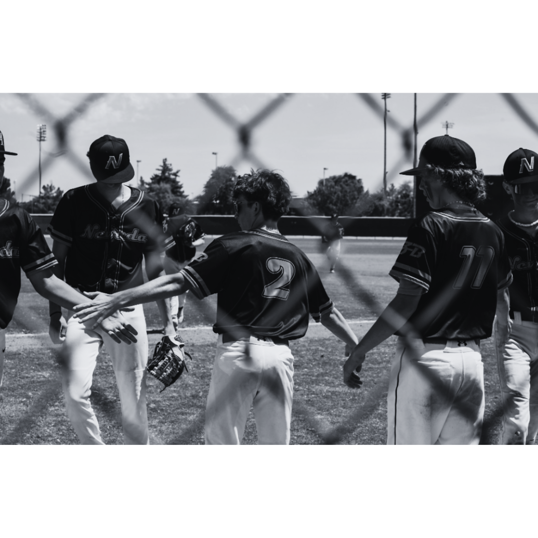 Baseball players in uniform huddling on the field during a game with a chain-link fence in the foreground.