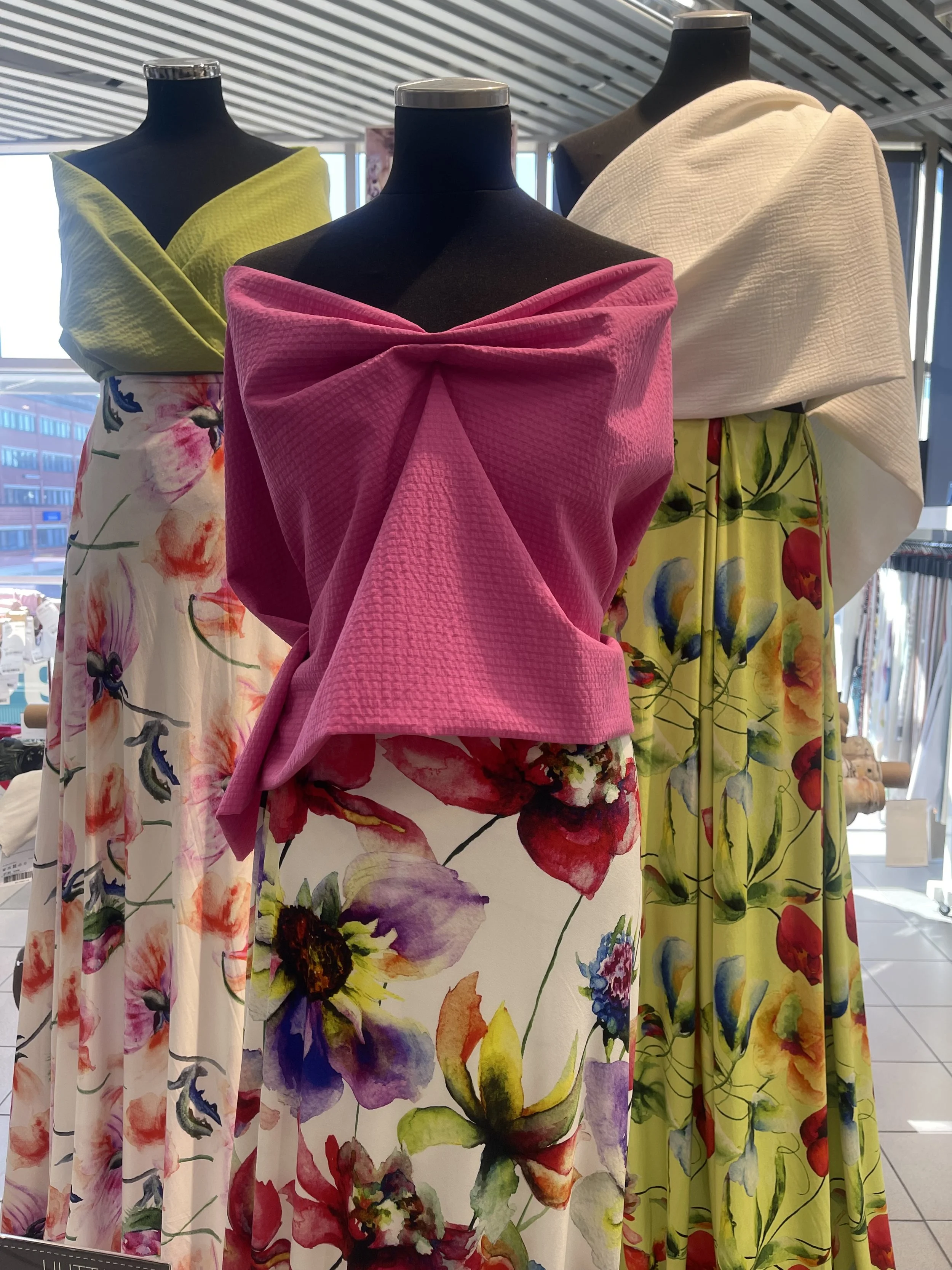 Four mannequins displaying colorful dresses with floral and textured fabric patterns in a store. cheekychk