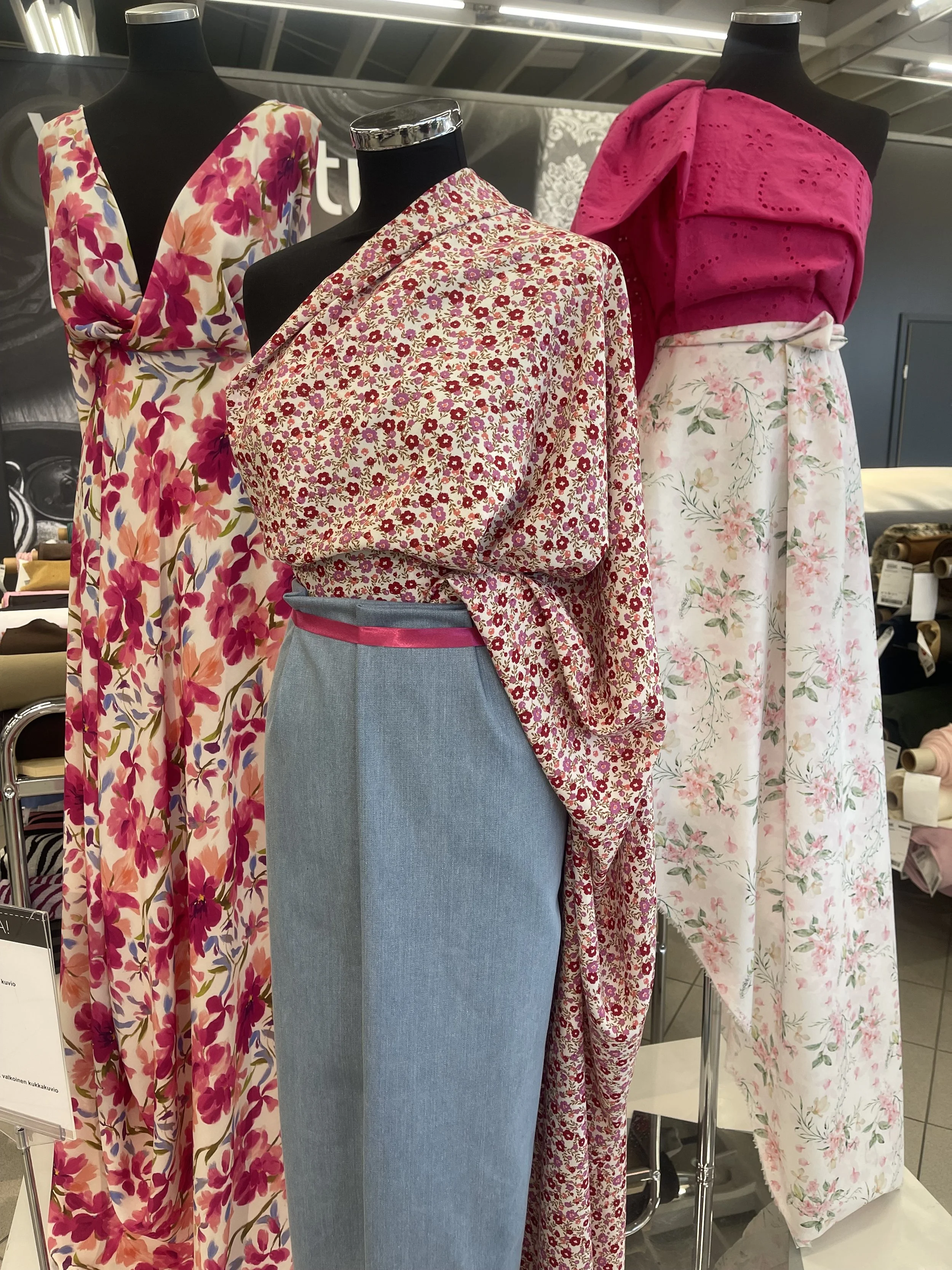 Mannequins dressed in floral clothing display in a store, with two mannequins wearing dresses with pink, red, and green floral patterns, and a skirt with a pink top and floral skirt. cheekychk