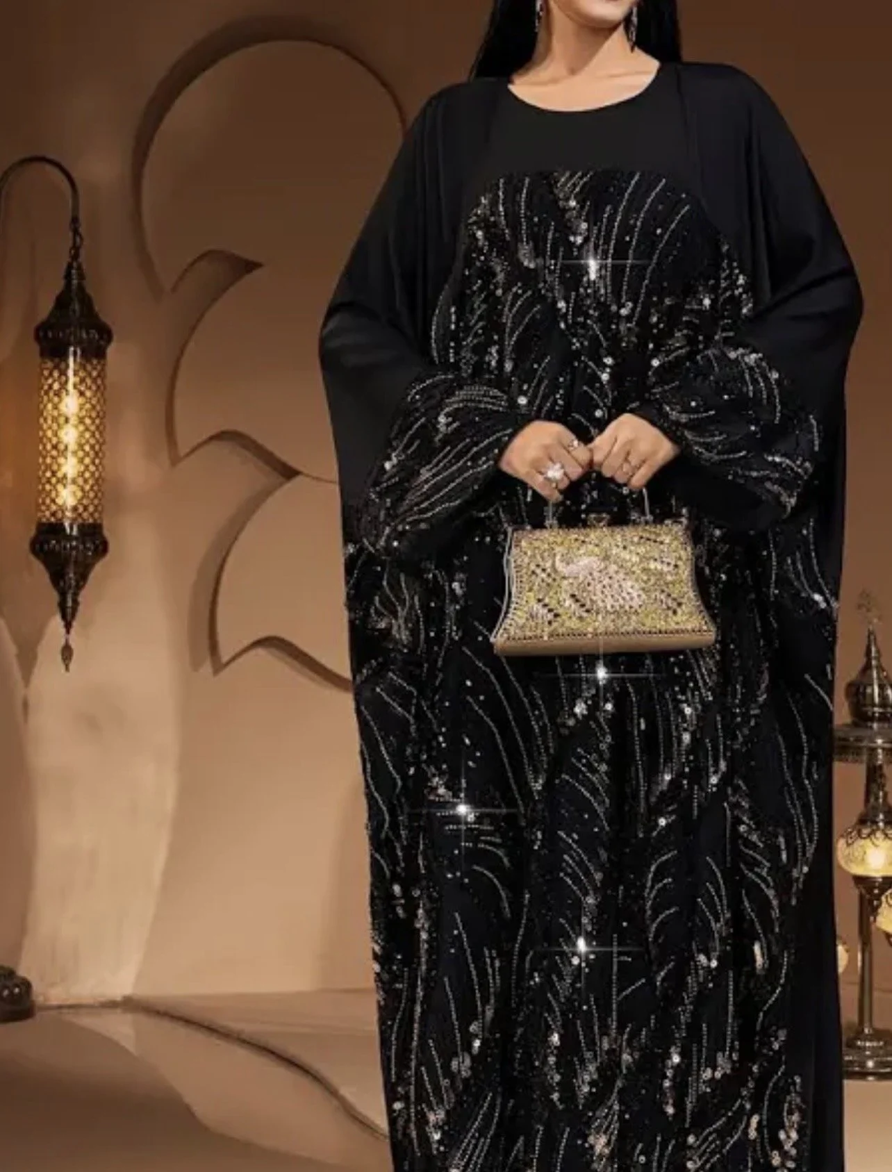 A woman in a black sequined dress holding a gold embellished clutch purse, standing in a room with Moroccan-style lanterns and wall decorations. cheekychk