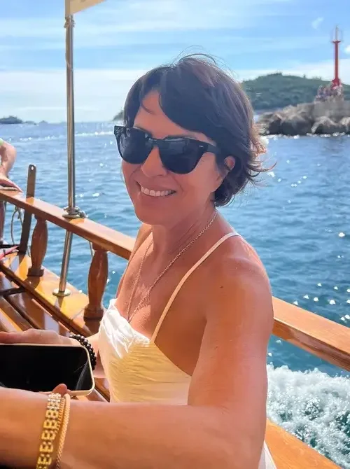 Smiling woman in sunglasses on boat with water and lighthouse in background