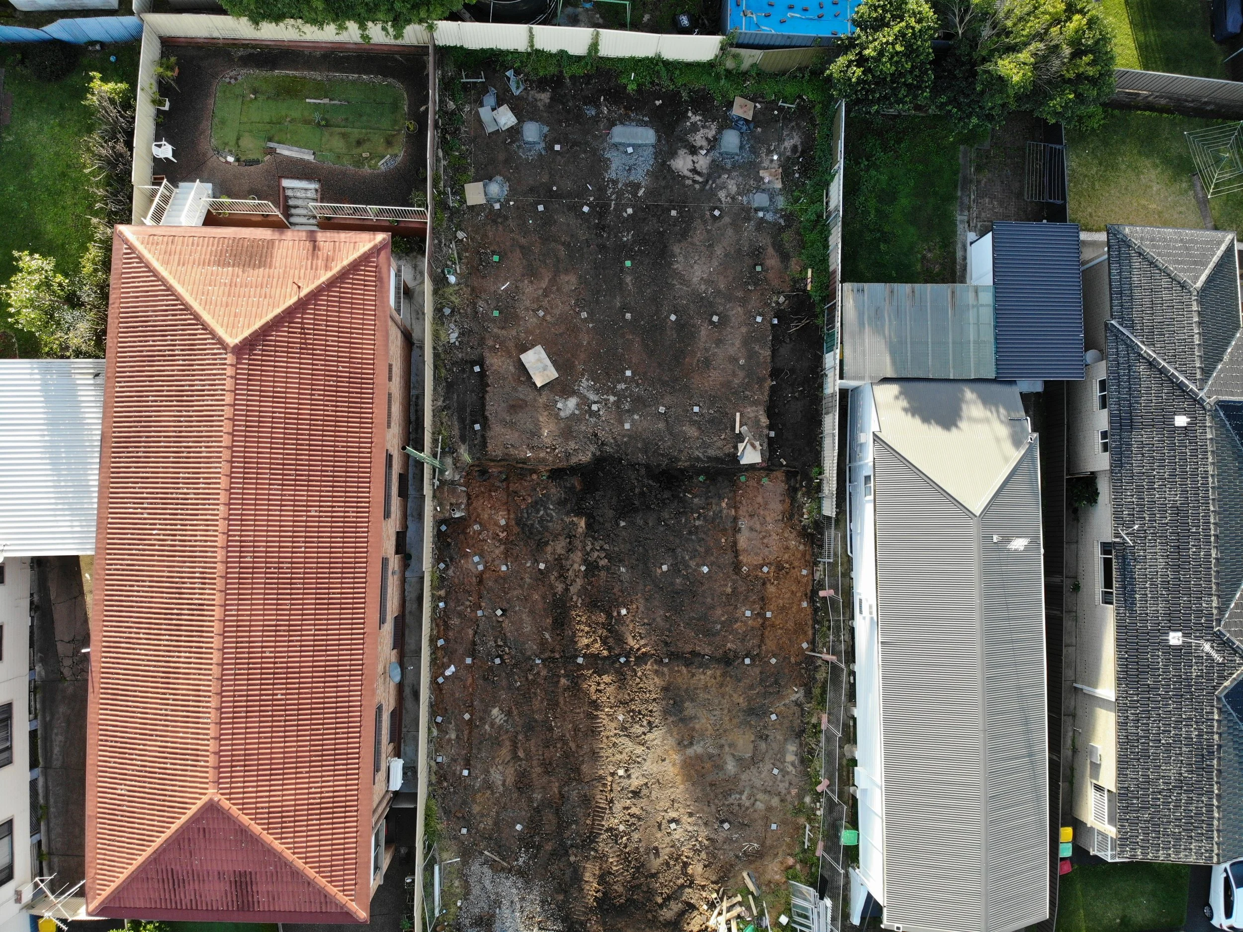 An aerial view of a backyard under renovation, with a large area of exposed dirt and construction debris 