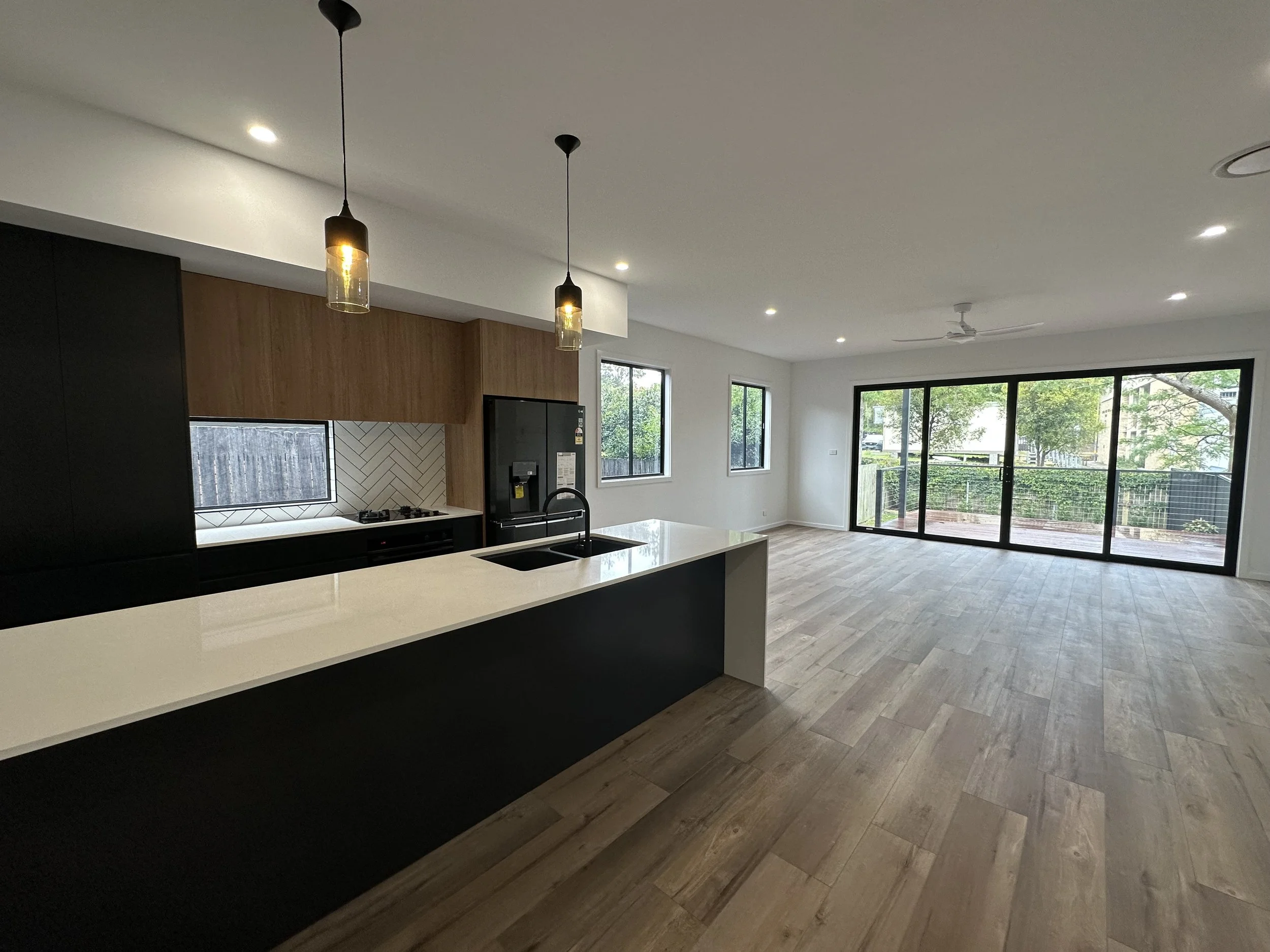 Modern open-concept living room and kitchen with large sliding glass doors leading to a balcony, hardwood floors, white walls, and ceiling lights.